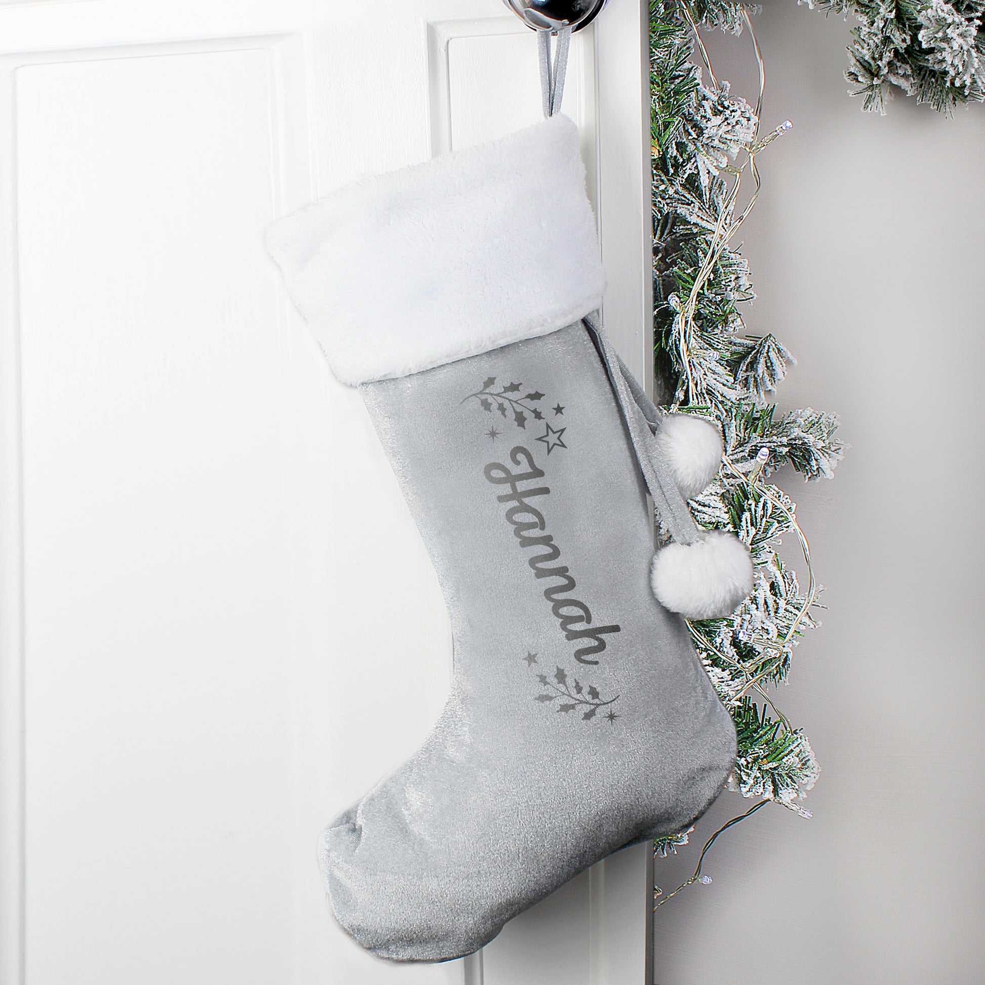 Gray Christmas stocking with white pom-poms hanging on a white door with decorative greenery.