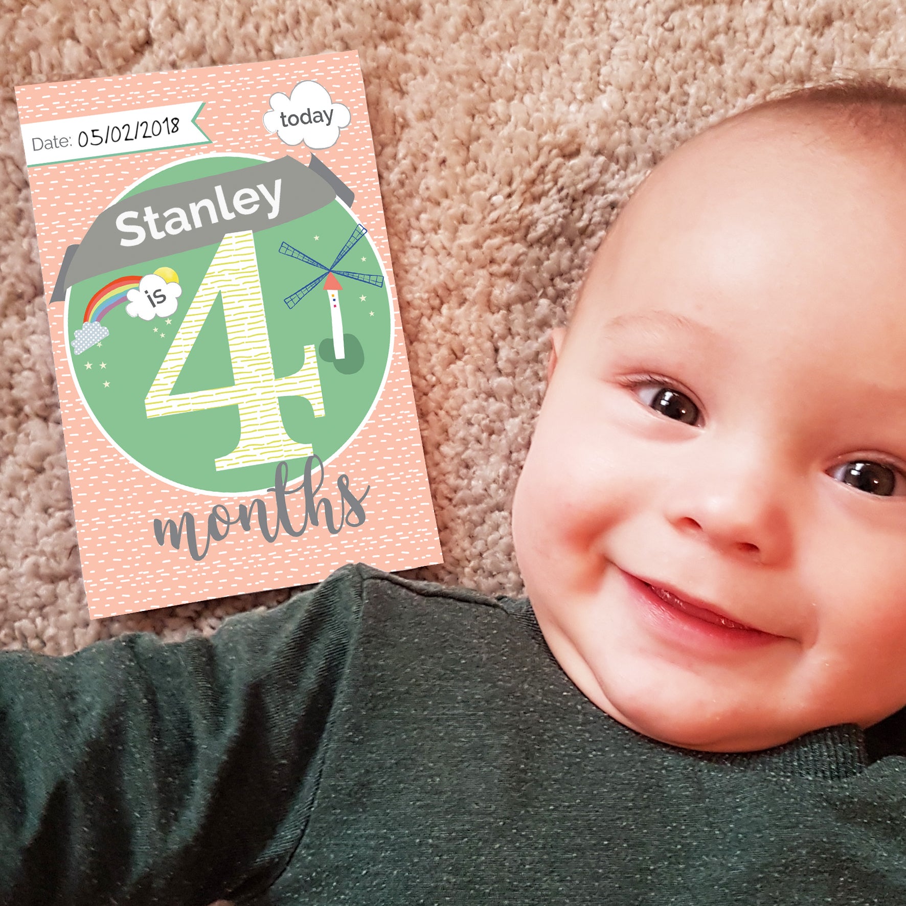 Baby lying on a carpet next to a milestone card celebrating 4 months.