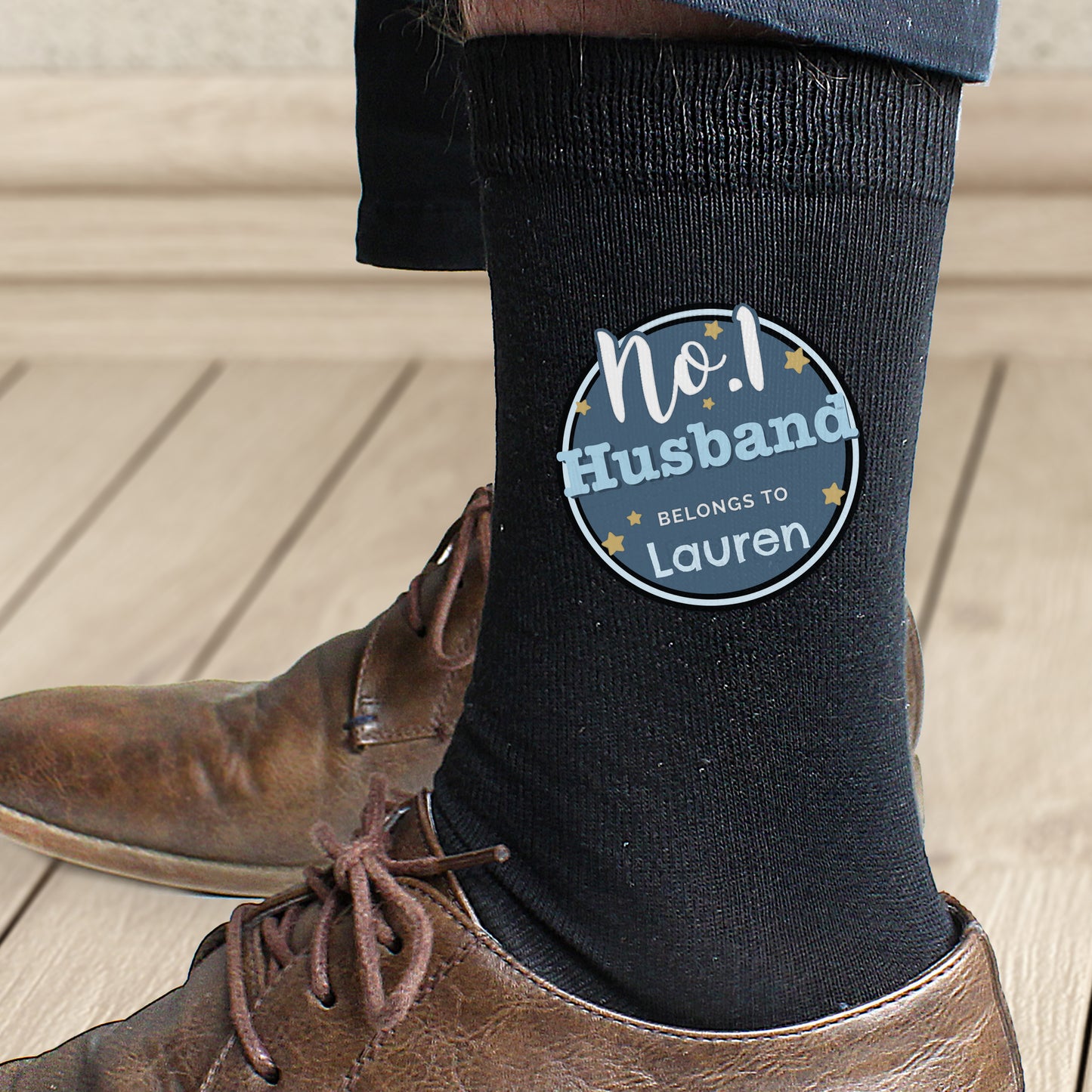 Black sock with a personalized label worn by a person on a wooden floor.