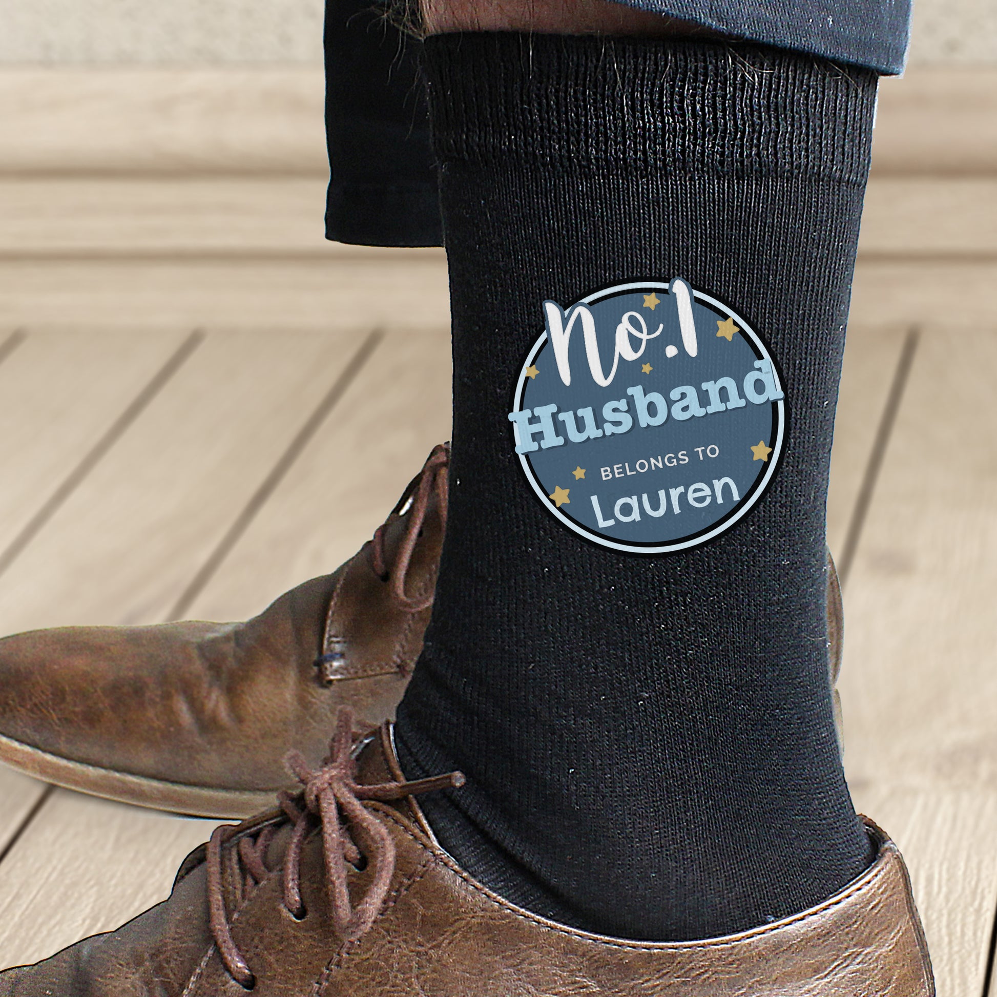 Black sock with a personalized label worn by a person on a wooden floor.