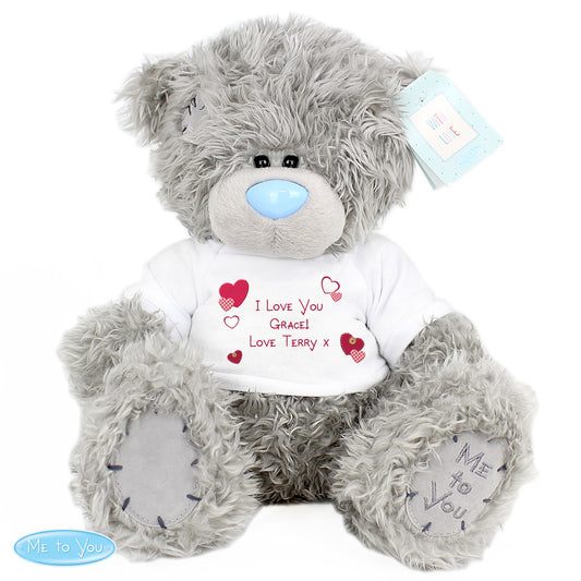 Grey teddy bear with a white shirt displaying personalised text, on a white background