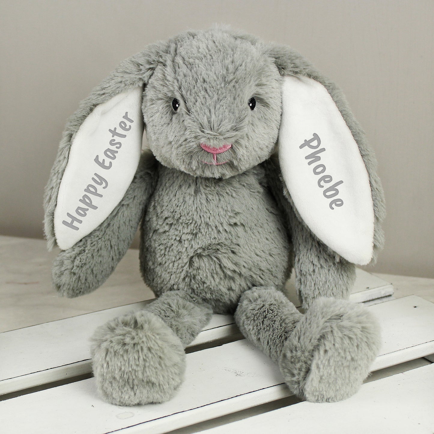 Grey plush bunny with 'Happy Easter' and 'Phoebe' on ears, sitting on a white surface.