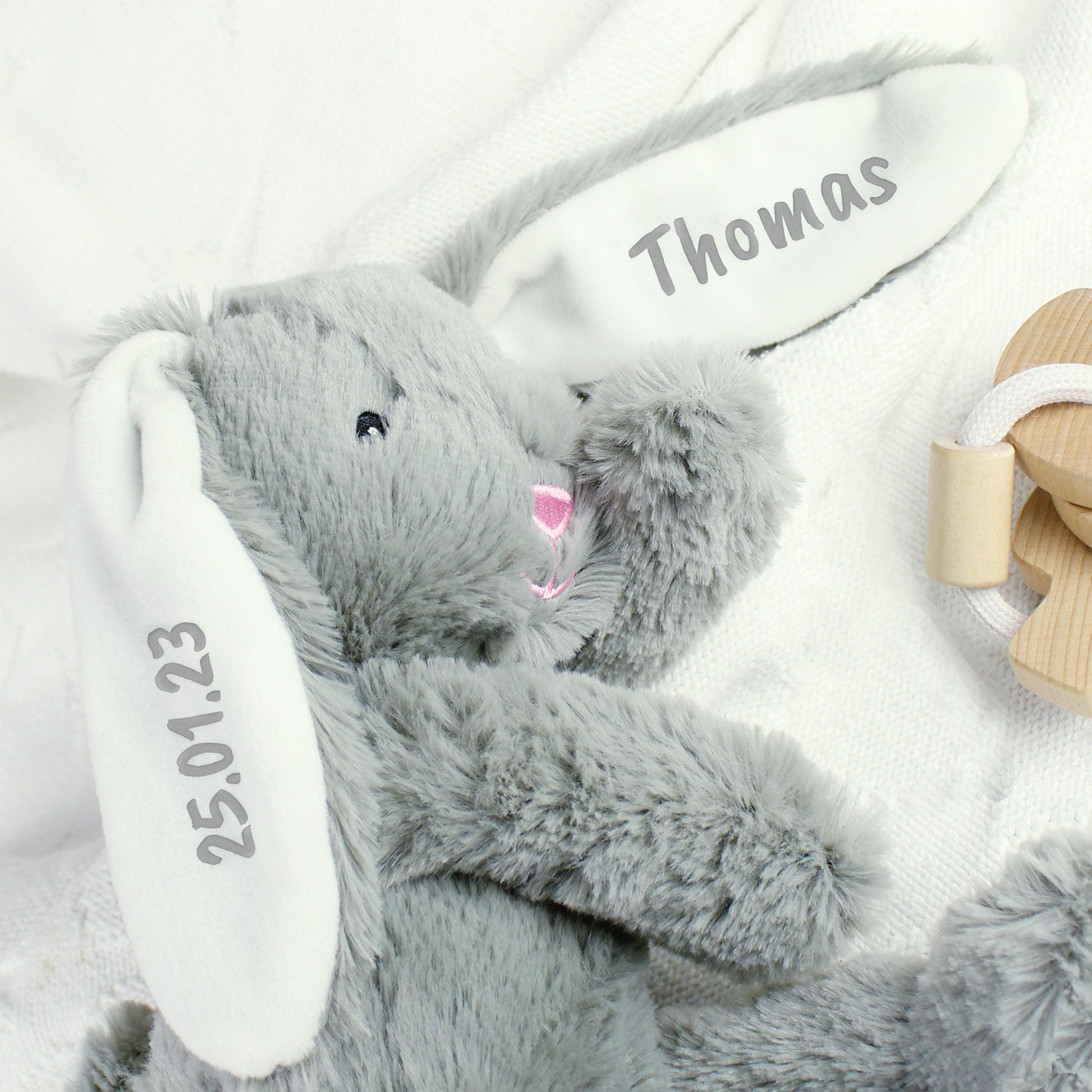 Grey plush bunny toy with 'Thomas' and a date on a white background