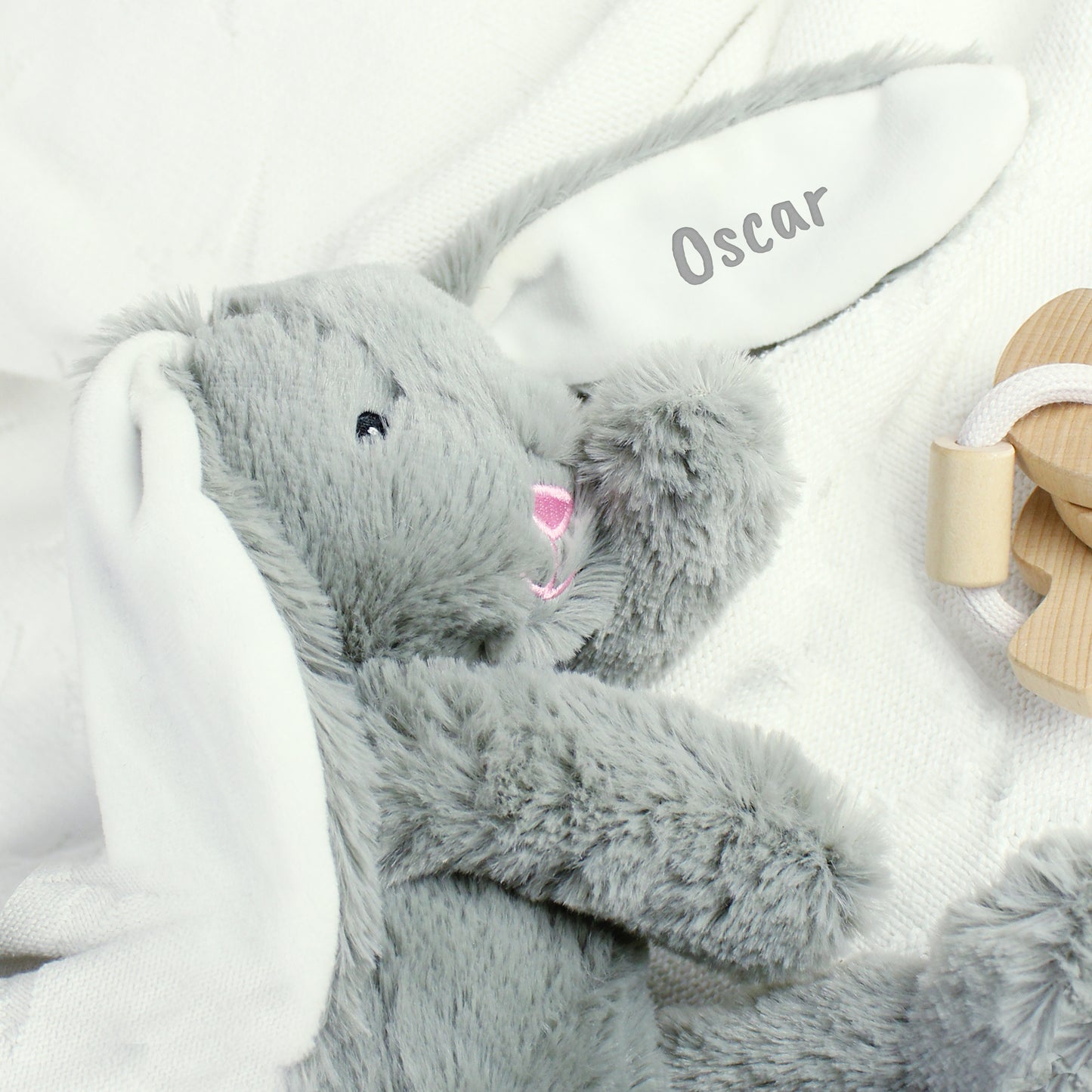 Grey plush bunny toy with a name tag on a white blanket