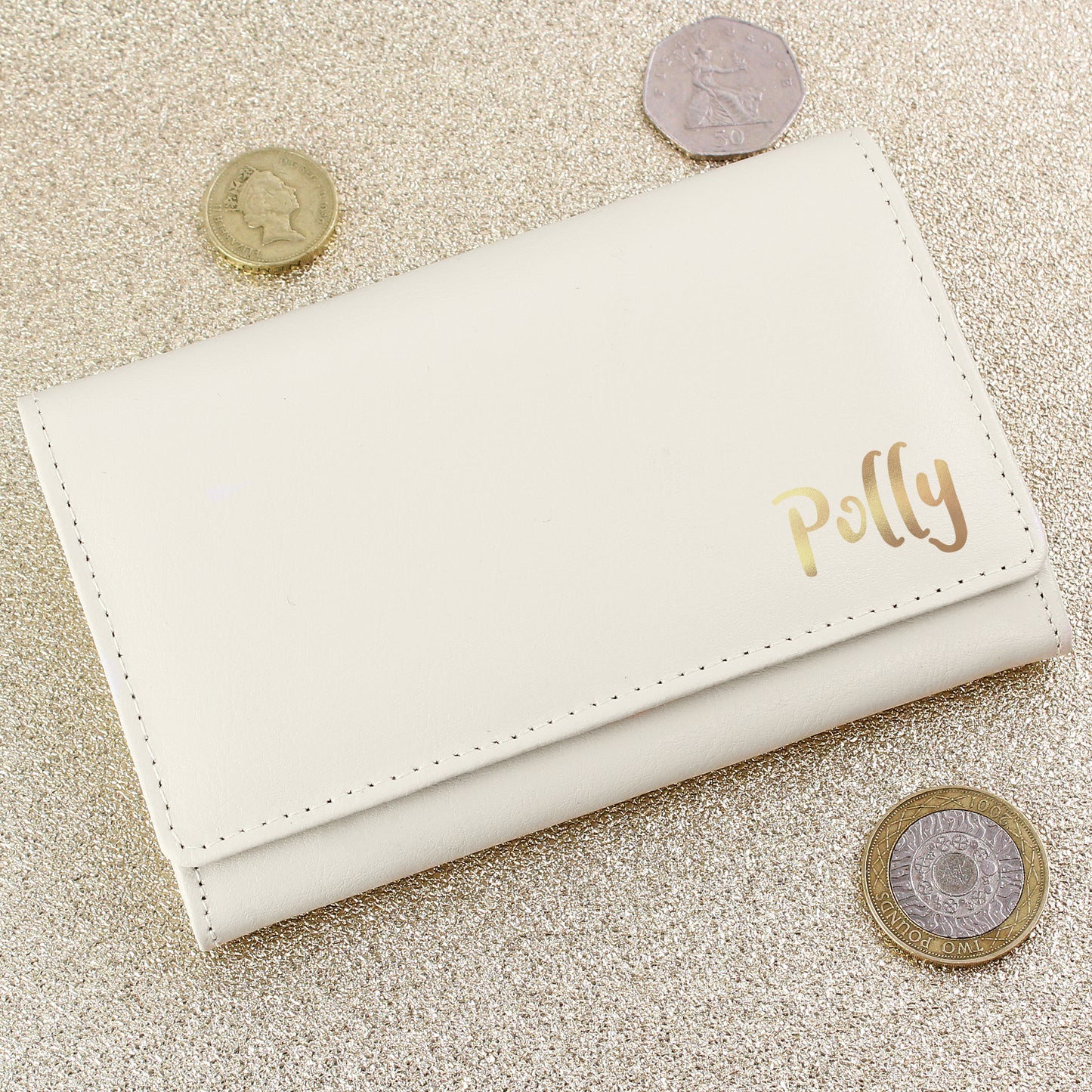 White wallet with 'Polly' engraving on a textured beige surface with coins around it.