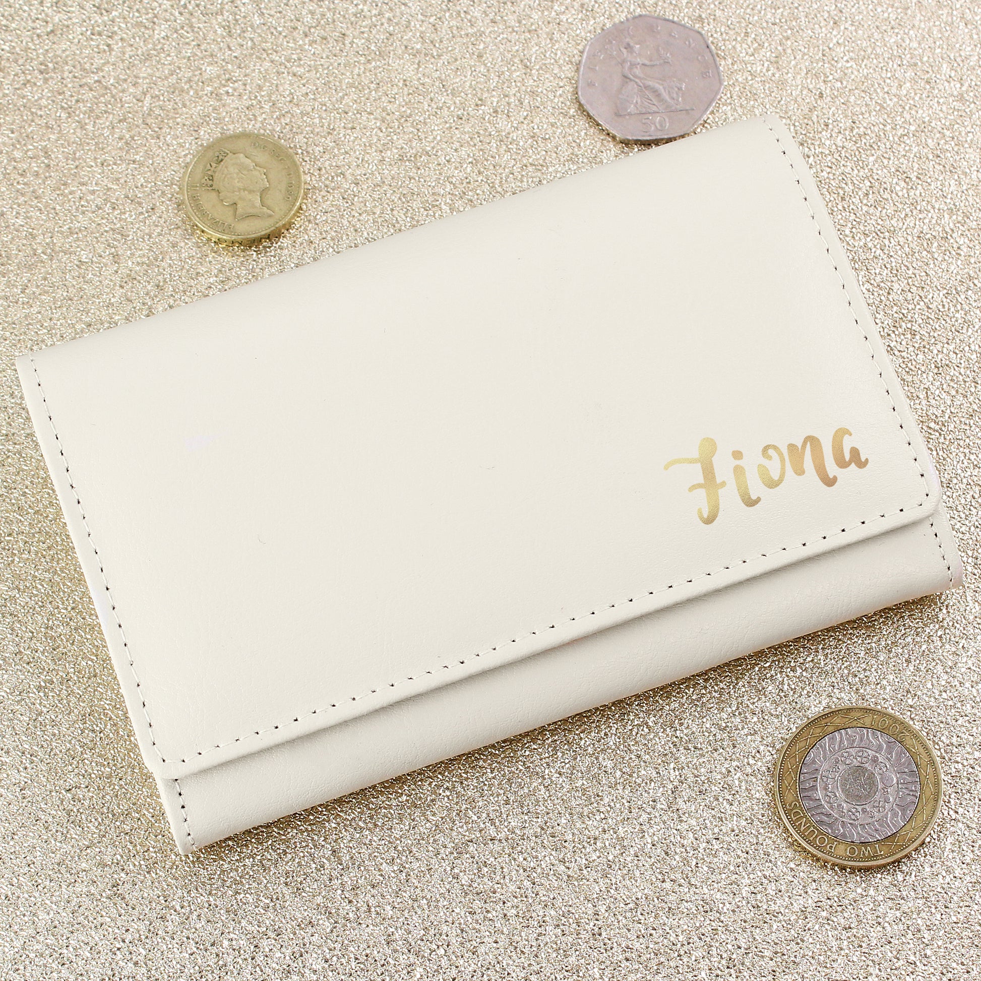 White wallet with 'Fiona' engraving on a glittery surface with coins around