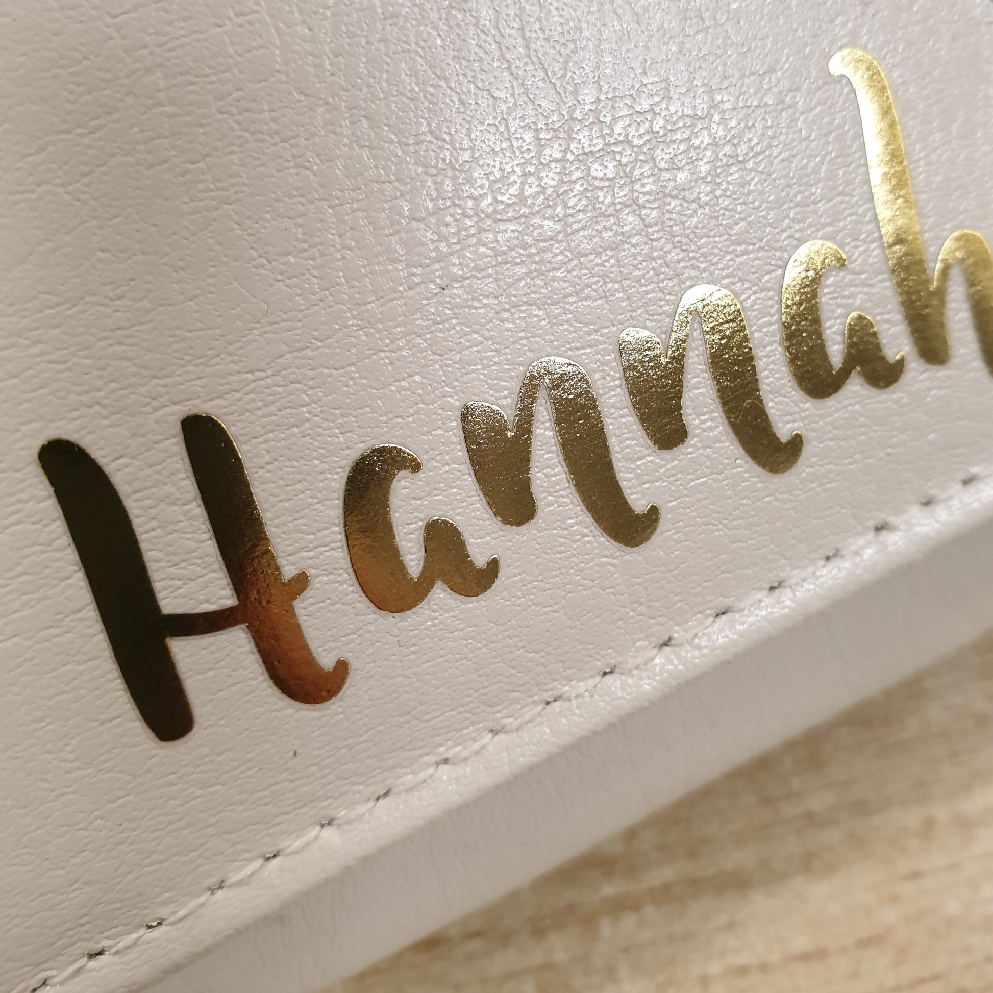 Close-up of a white leather product with 'Hannah' embossed in gold.