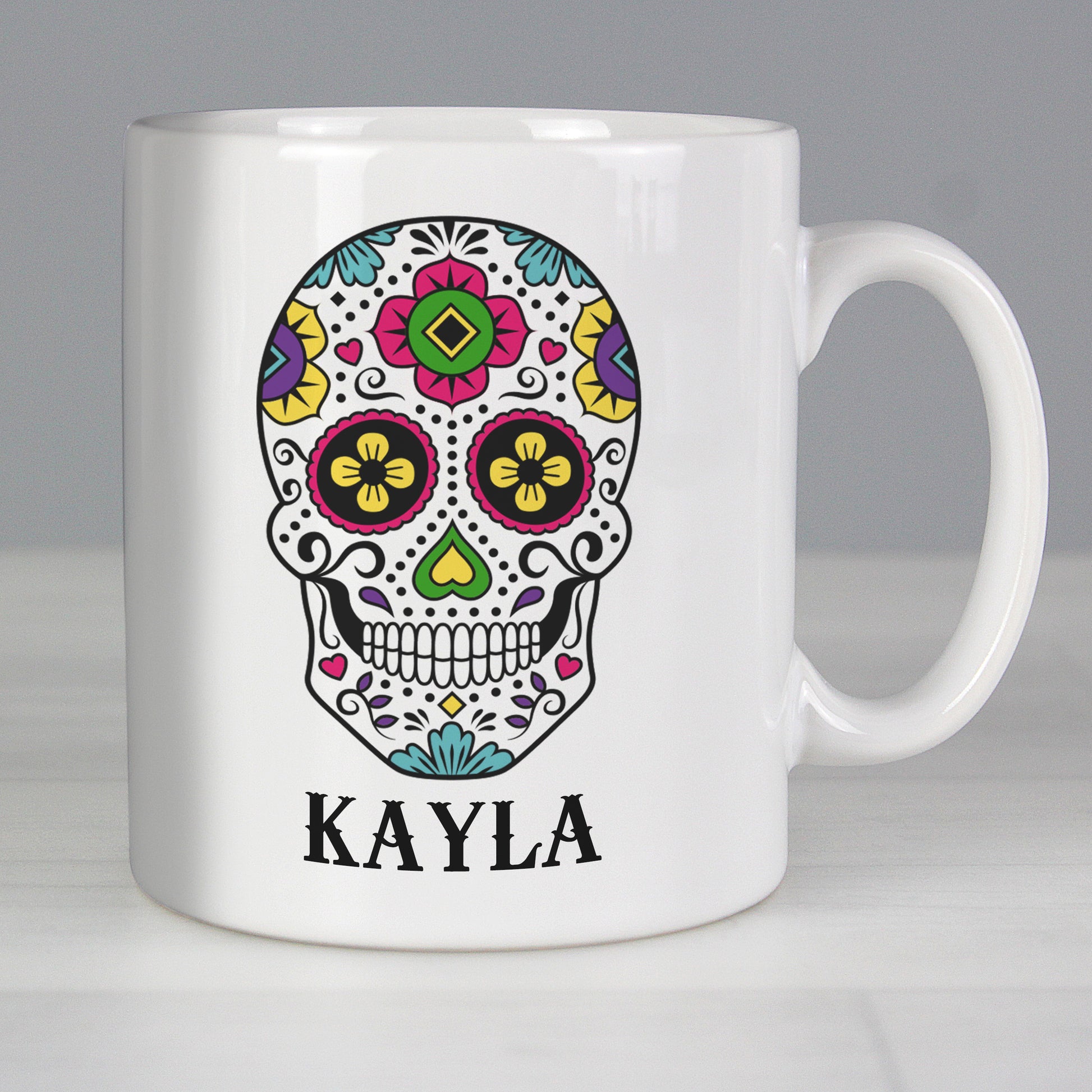White mug with a colorful skull design and the name 'Kayla' on a grey background