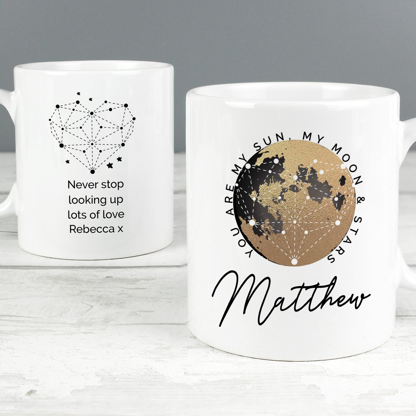 Two white mugs with star constellation designs and personalised text on a grey background.