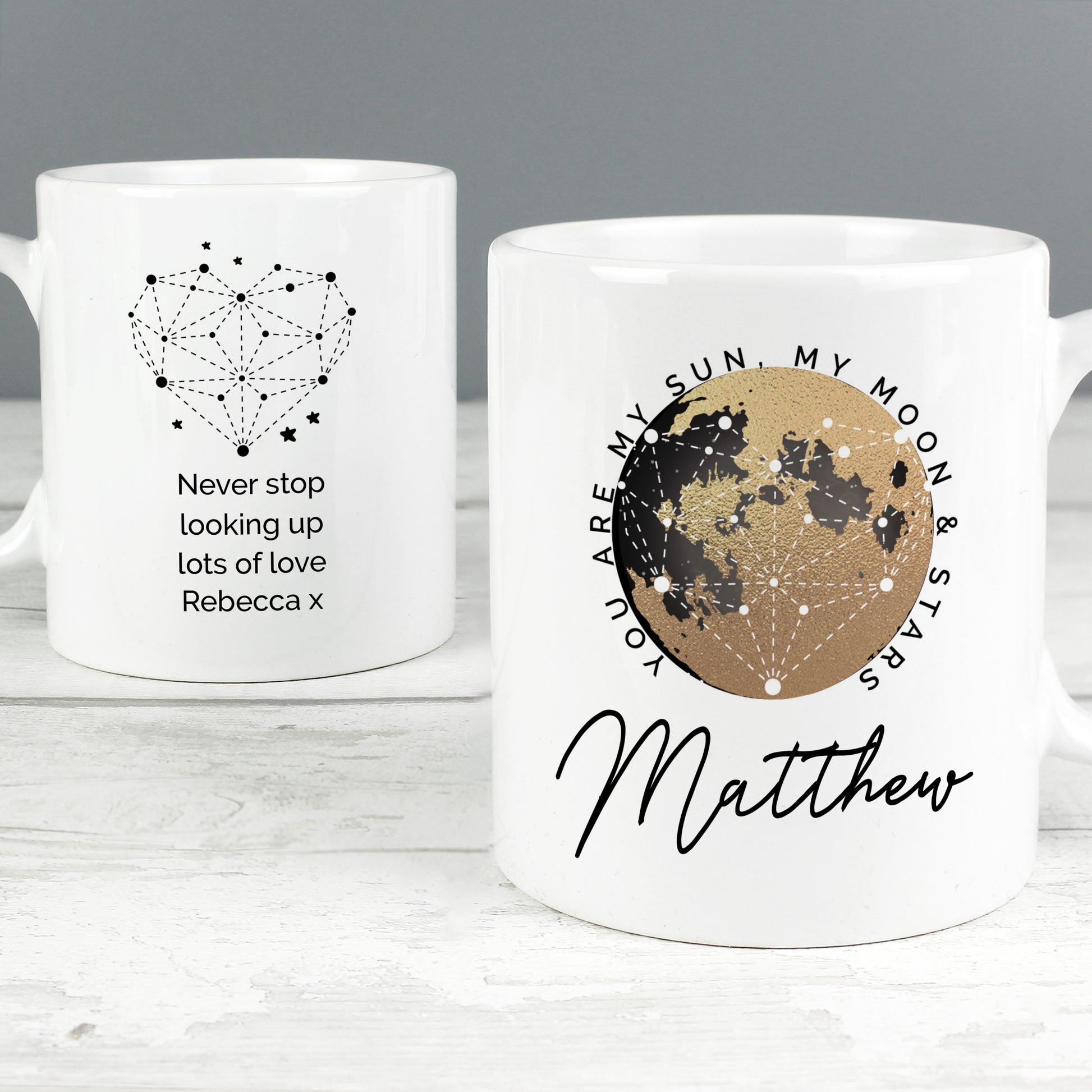 Two white mugs with star constellation designs and personalised text on a grey background.
