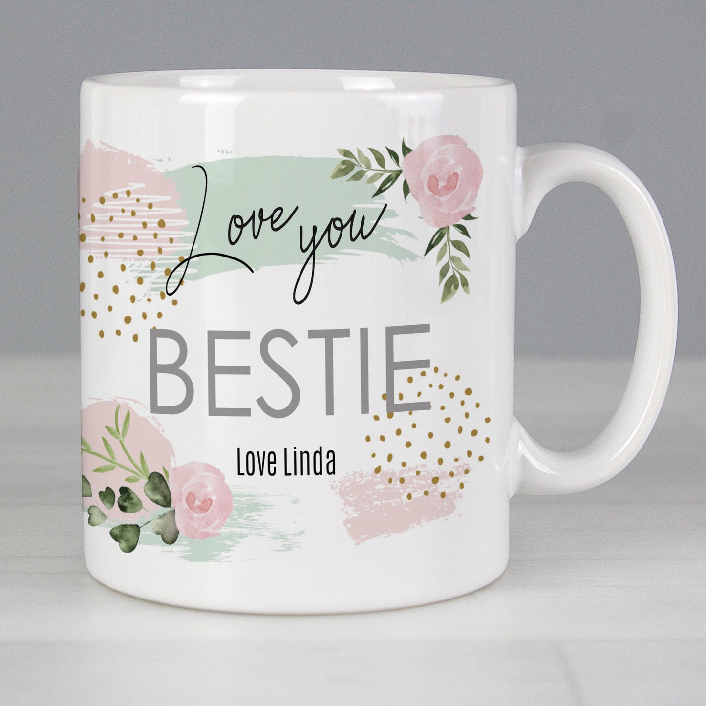 White mug with floral design and text 'Love you BESTIE Love Linda' on a grey background