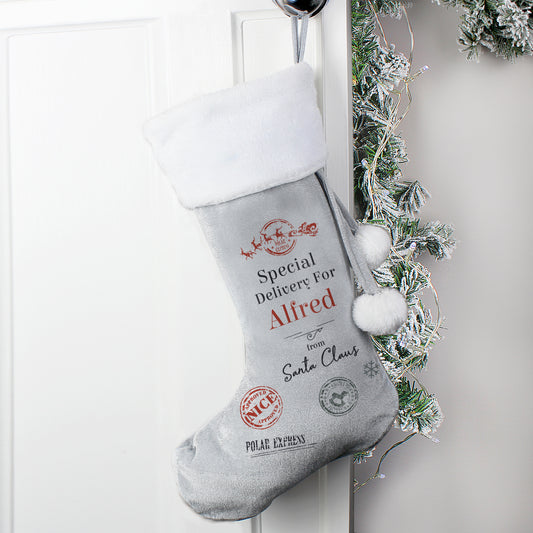 Grey Christmas stocking with personalised text hanging on a white door with festive decorations.