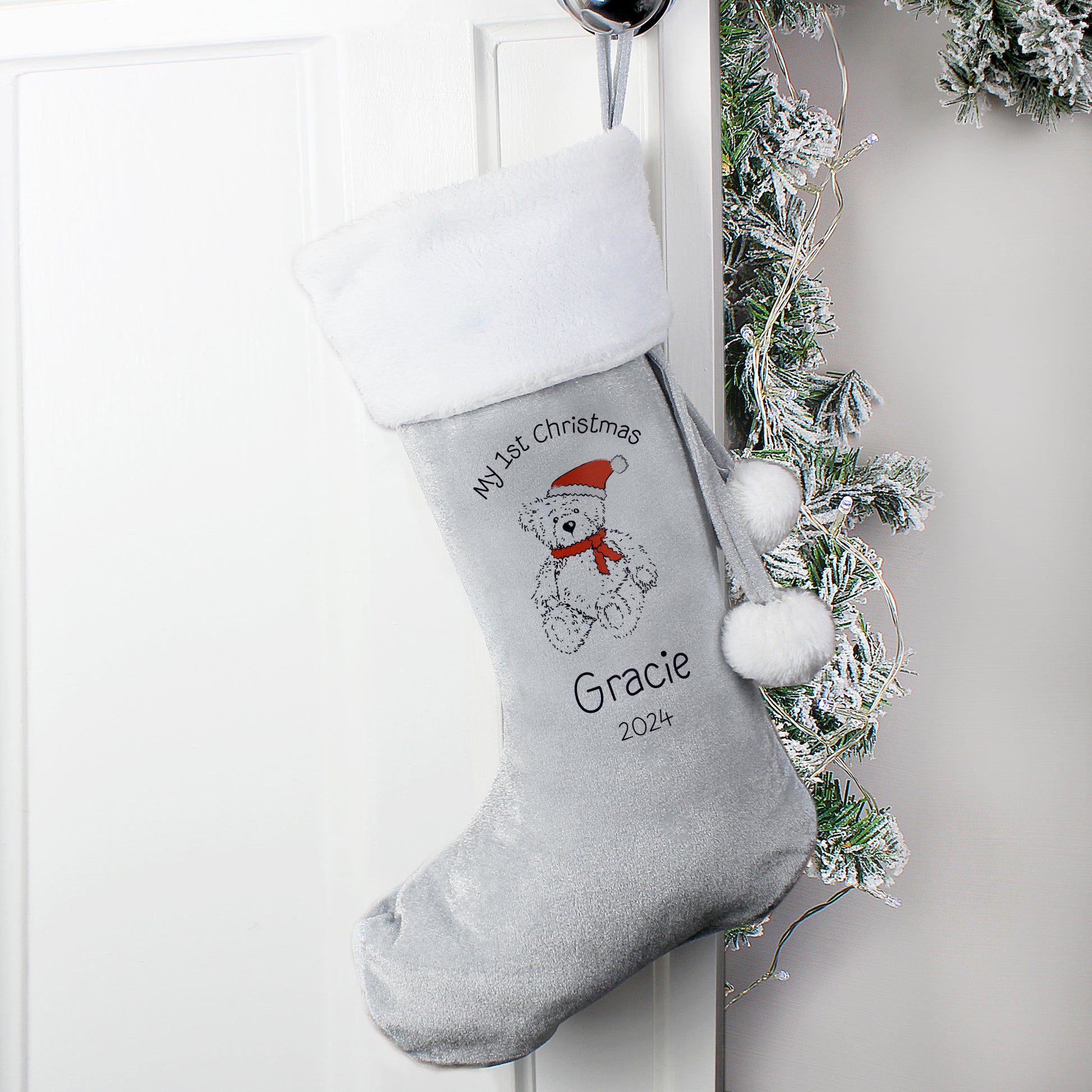Personalised Christmas stocking with a teddy bear design and text, hanging on a white door with festive decorations.