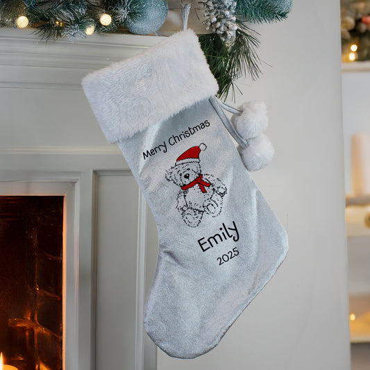 Personalised Christmas stocking with teddy bear design and text, hanging by a fireplace.