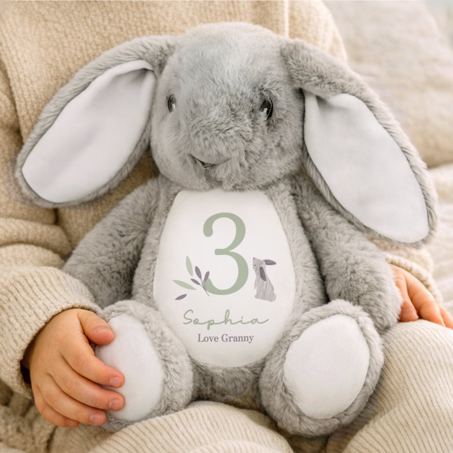 Grey plush bunny toy with a personalised label held by a child
