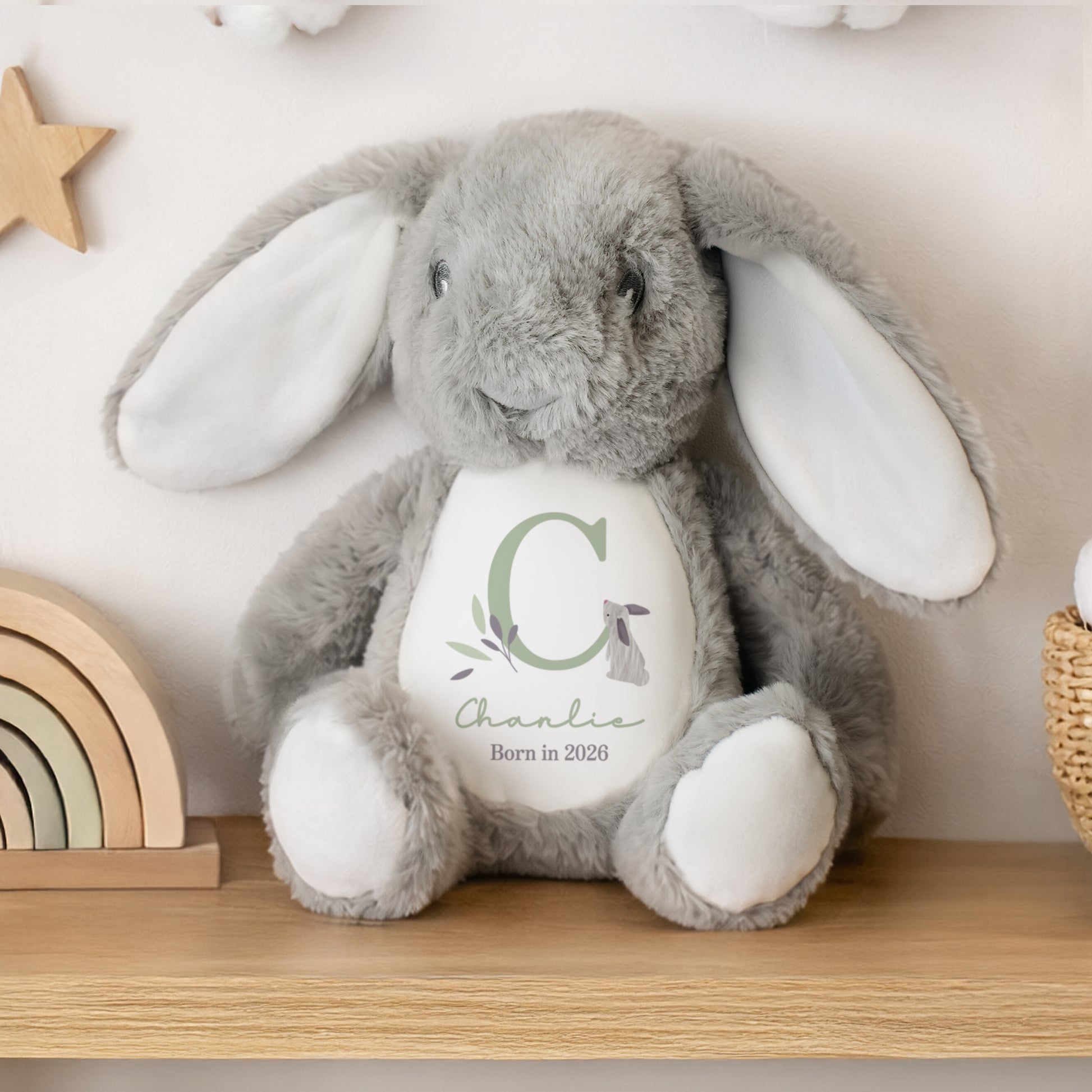 Grey personalised plush bunny with a white belly featuring text and a letter 'C' on a wooden shelf.