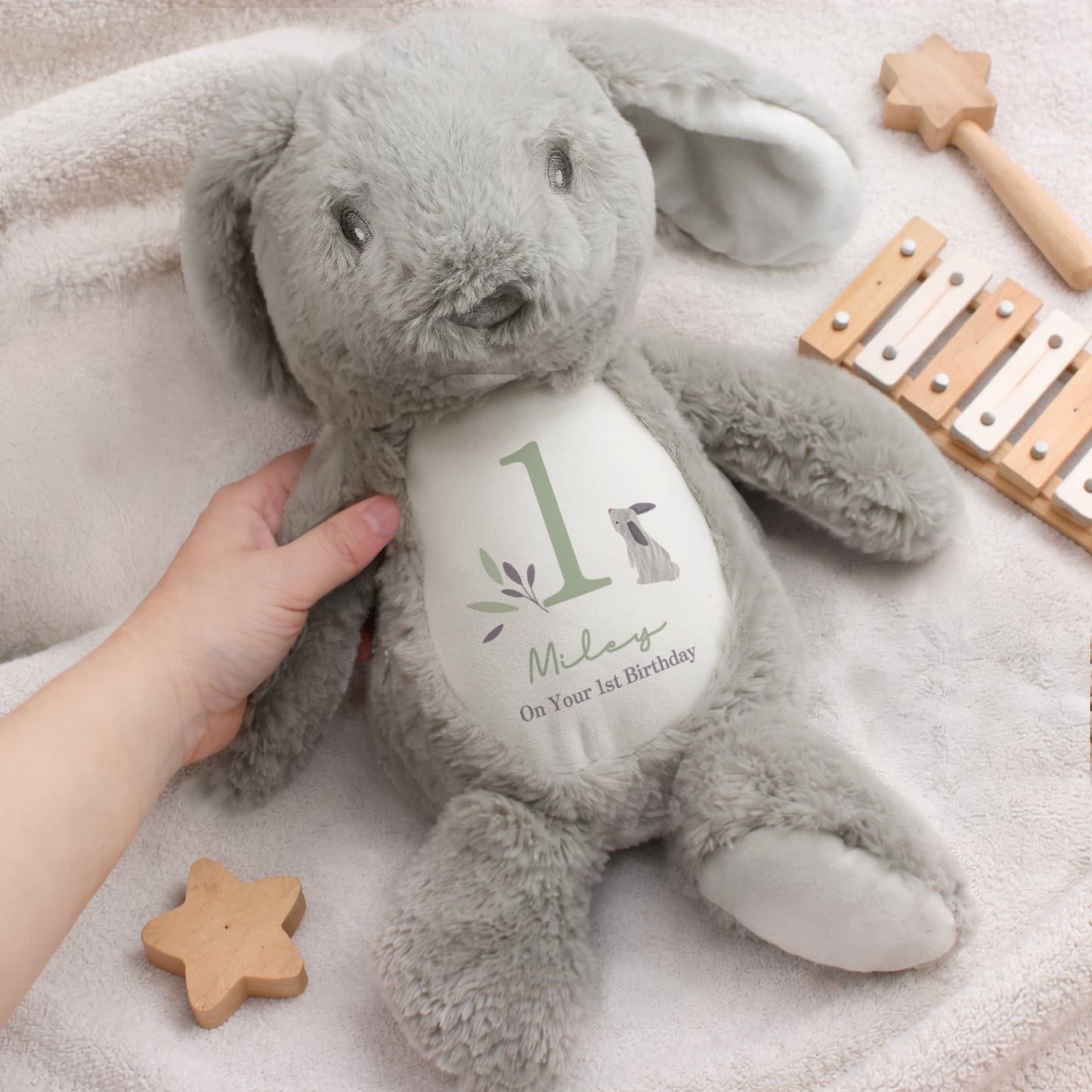 Grey plush bunny with a heart-shaped tag on a soft surface with wooden toys.