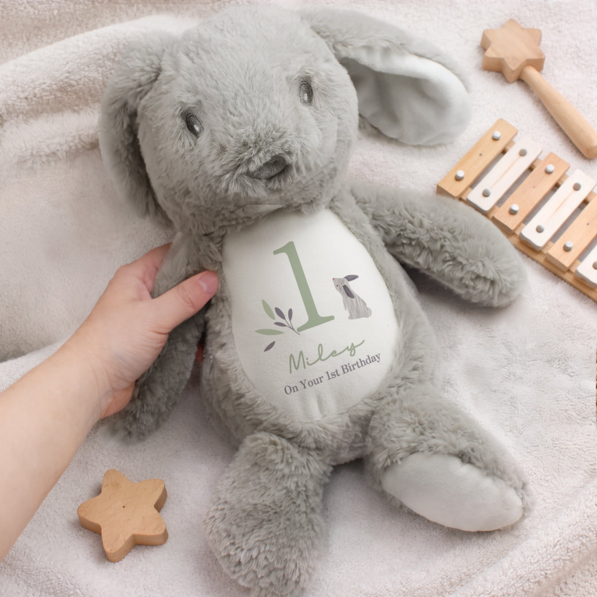 Grey plush bunny with a heart-shaped tag on a soft surface with wooden toys.