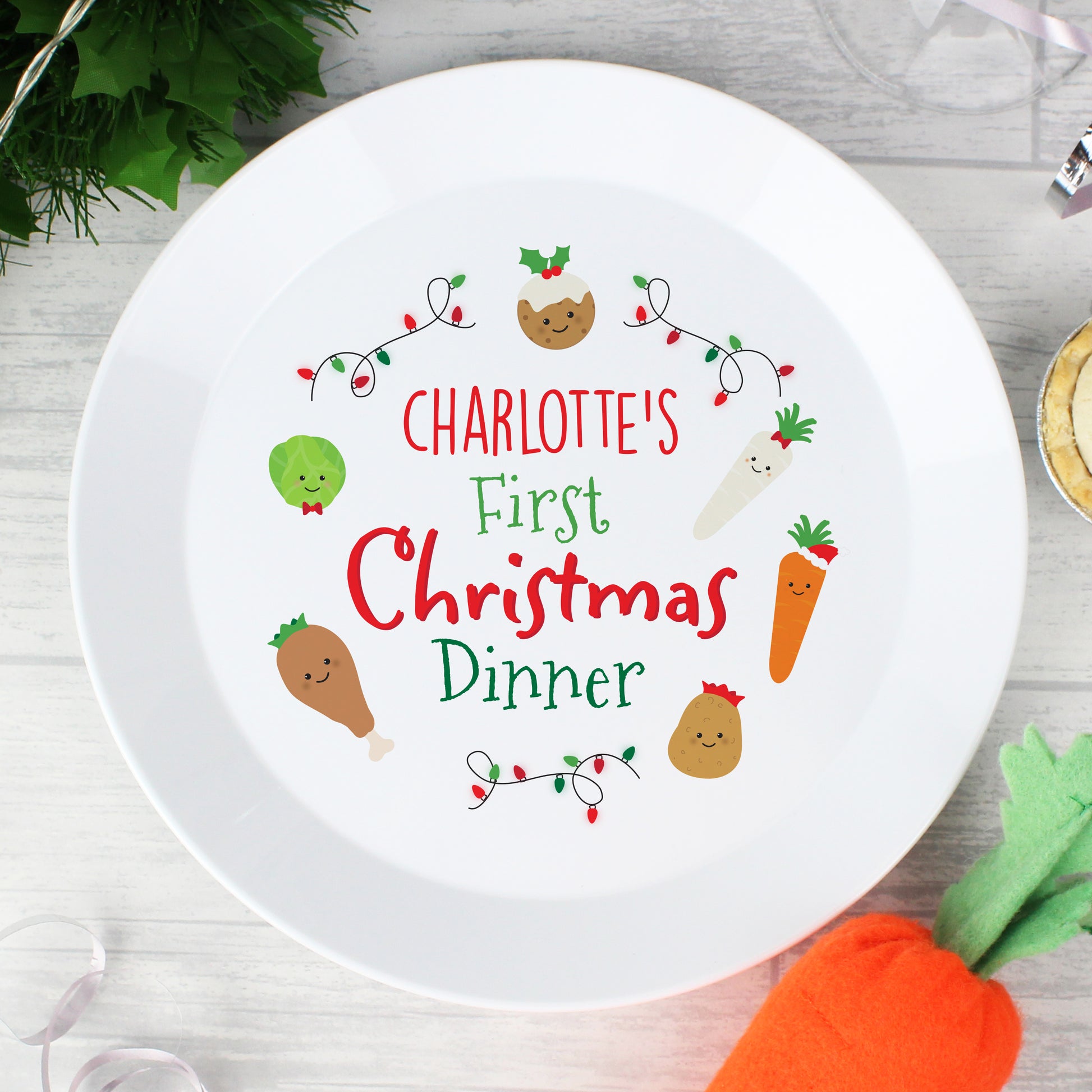 White plate with 'Charlotte's First Christmas Dinner' text and festive illustrations on a wooden surface.