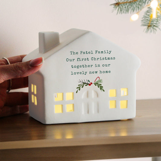 White house-shaped light with personalised message on a wooden surface with Christmas decorations.