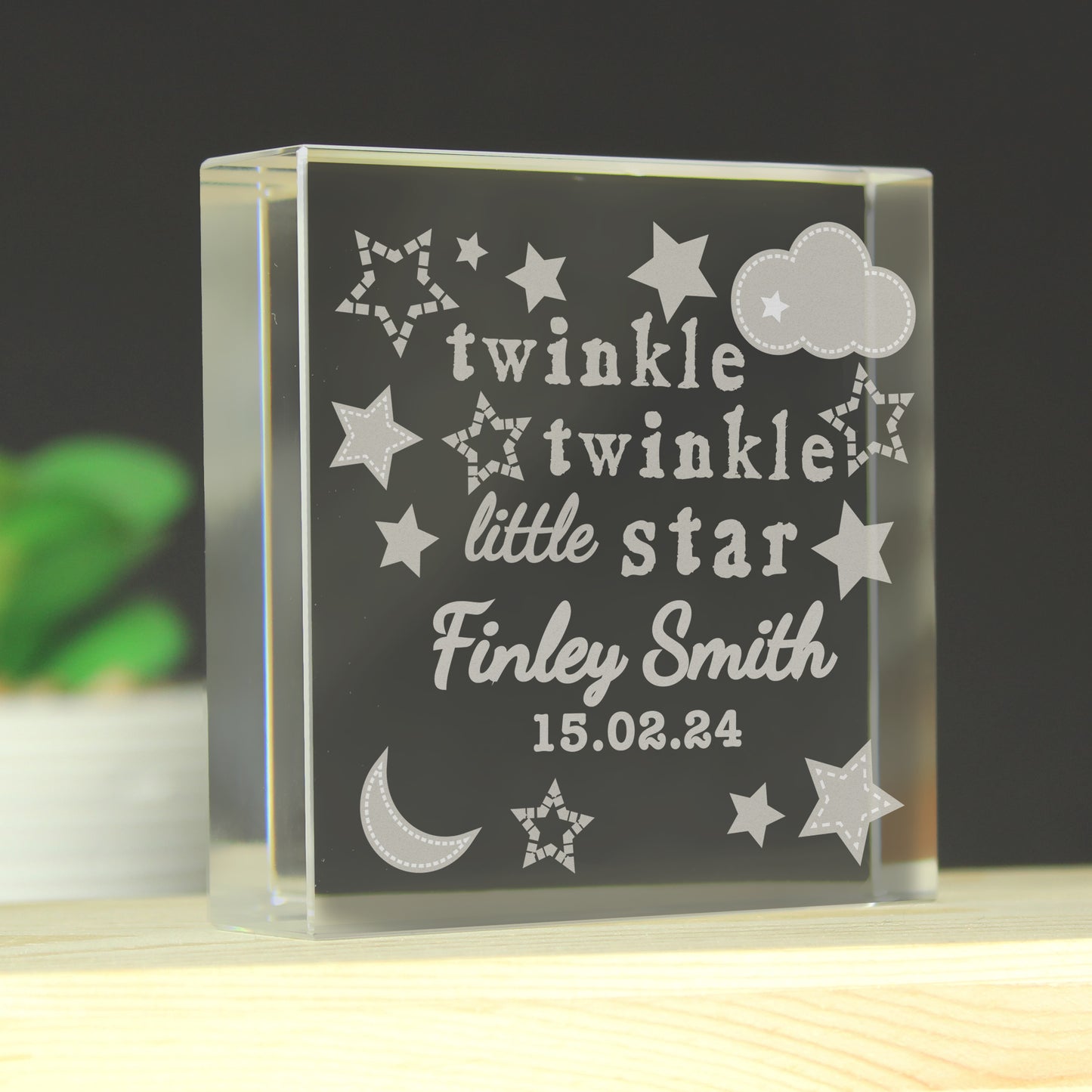 Personalised glass block with engraved text and star designs on a dark background