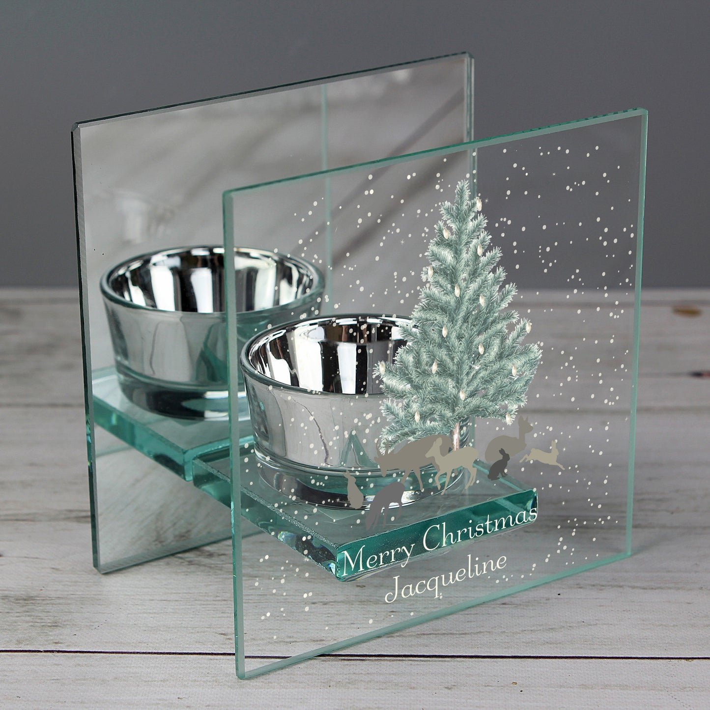 Decorative glass candle holder with silver bowl and a Christmas scene on a wooden surface.