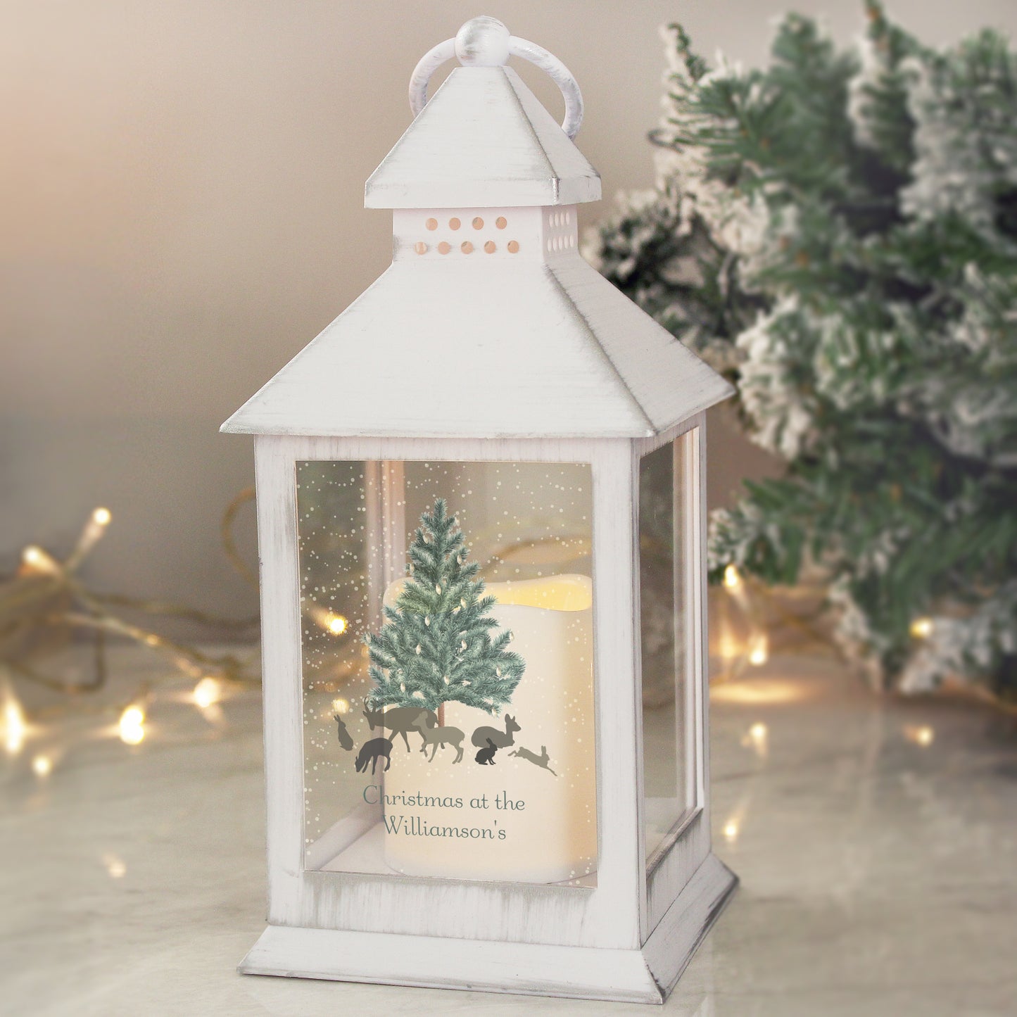White lantern with Christmas scene and tree, surrounded by festive lights and decorations.