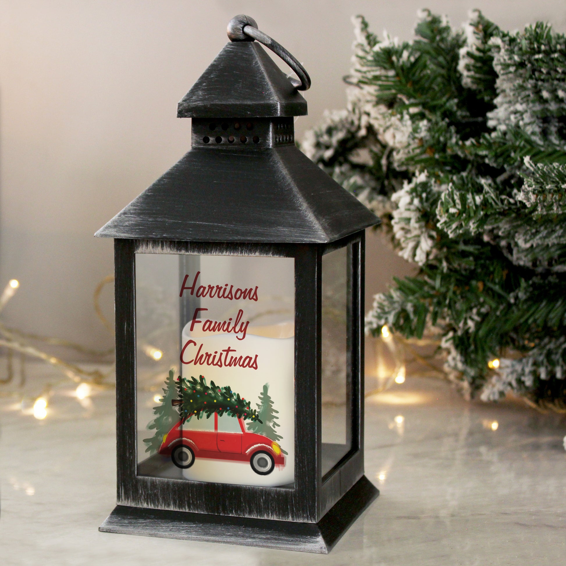 Decorative lantern with a Christmas scene and 'Harrisons Family Christmas' text, placed in front of a snowy tree.