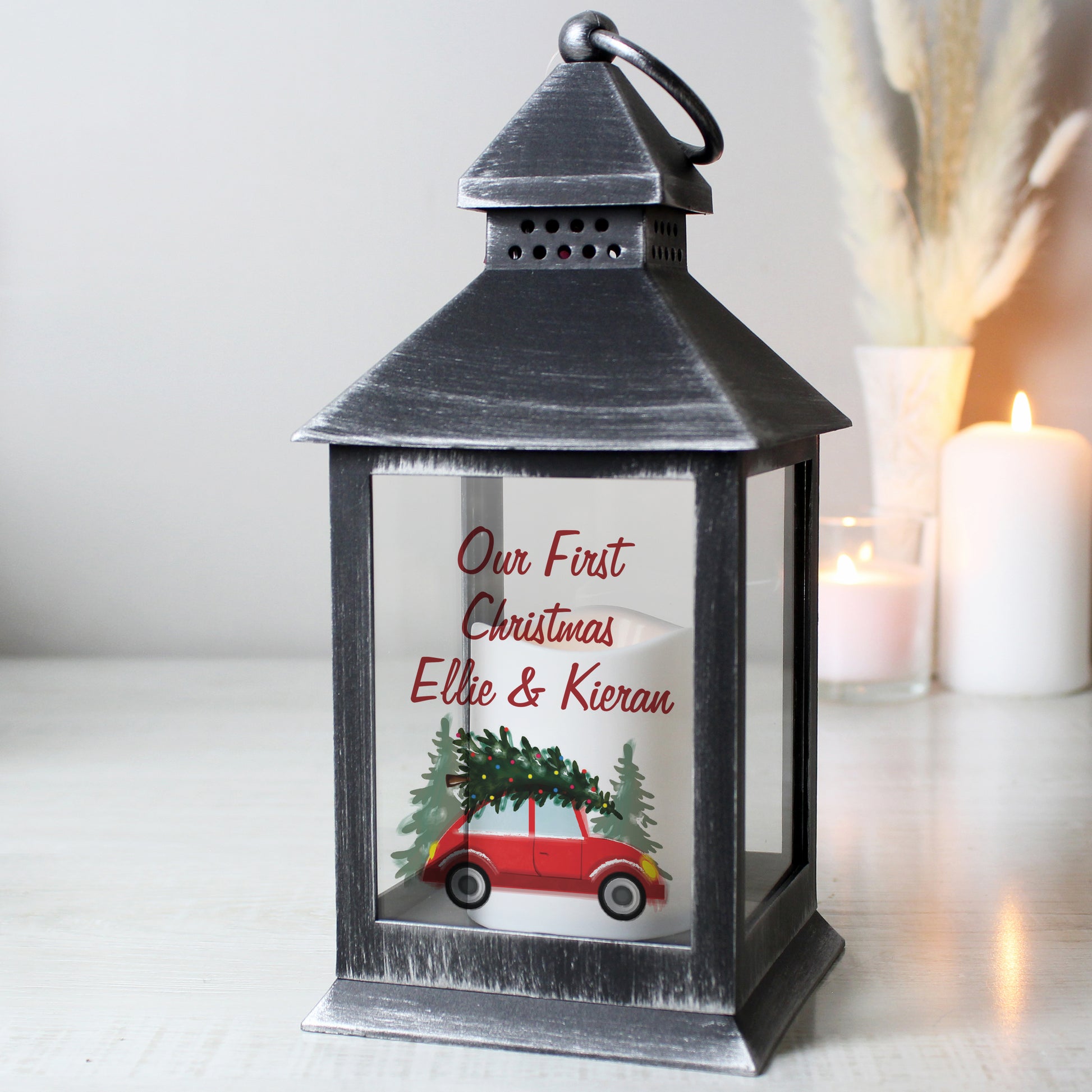Decorative lantern with 'Our First Christmas Ellie & Kieran' text and car with tree illustration.