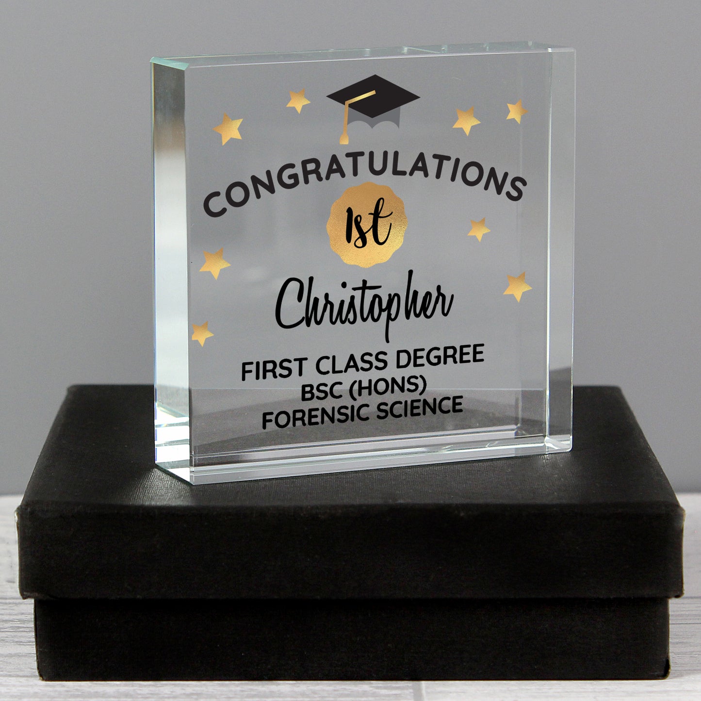 Glass graduation award with engraved text on a black box against a grey background
