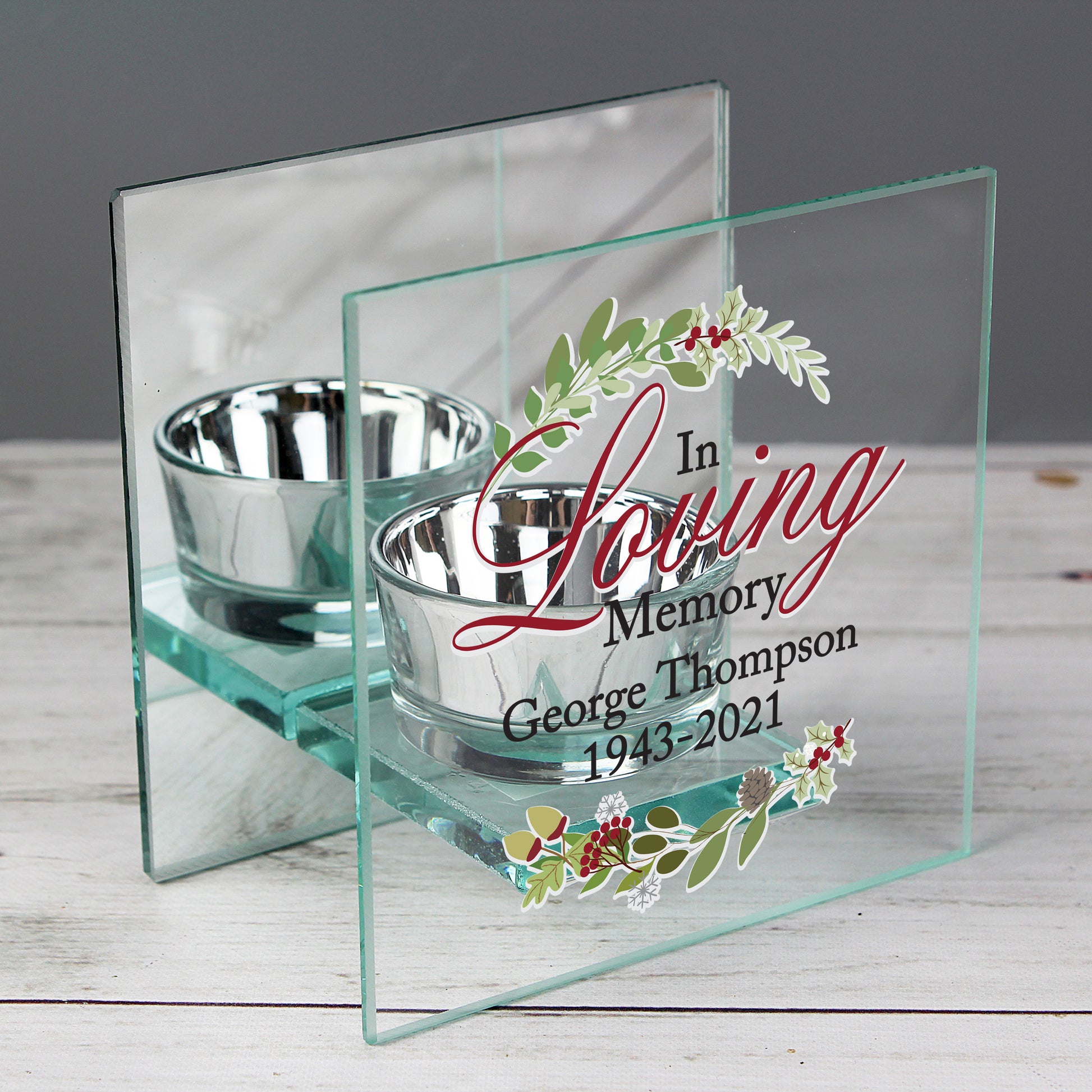 Glass memorial holder with two silver bowls and engraved text on a wooden surface.