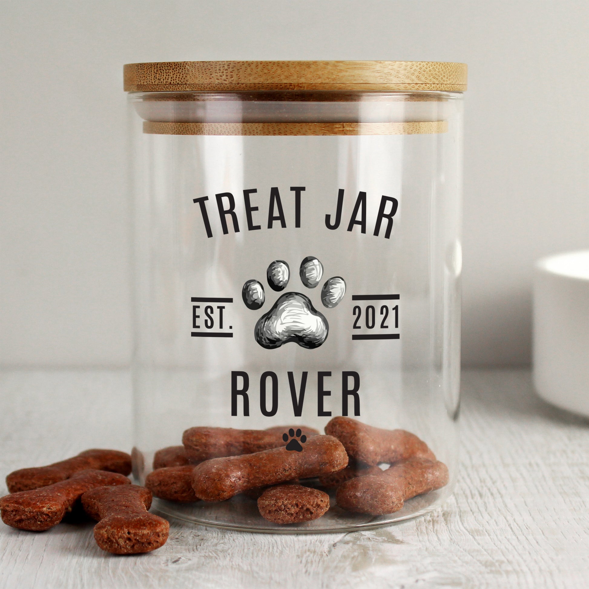 Clear treat jar with wooden lid labeled 'Treat Jar' and 'Rover' on a light surface.