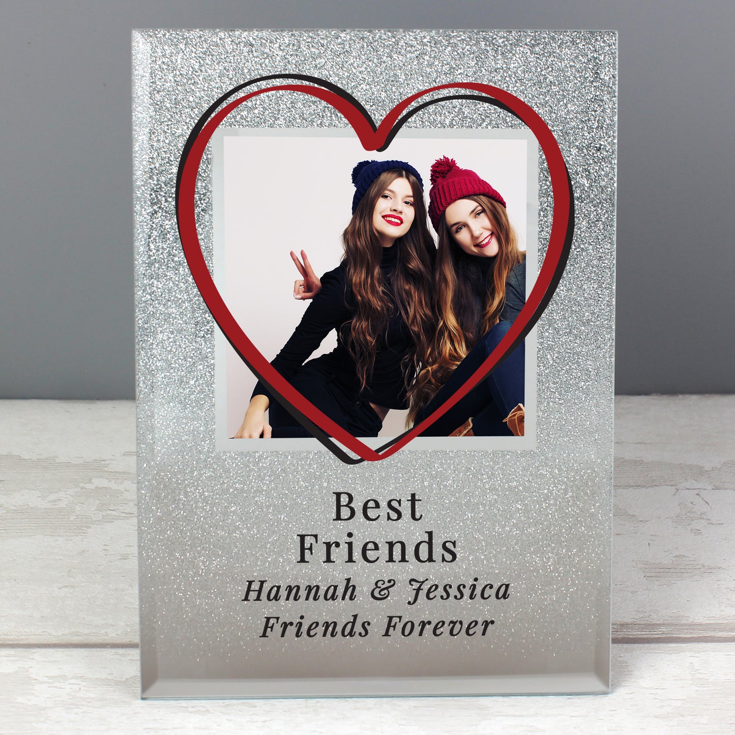 Heart-shaped photo frame with a photo of two people and personalised text 'Best Friends Hannah & Jessica Friends Forever' on a grey background.