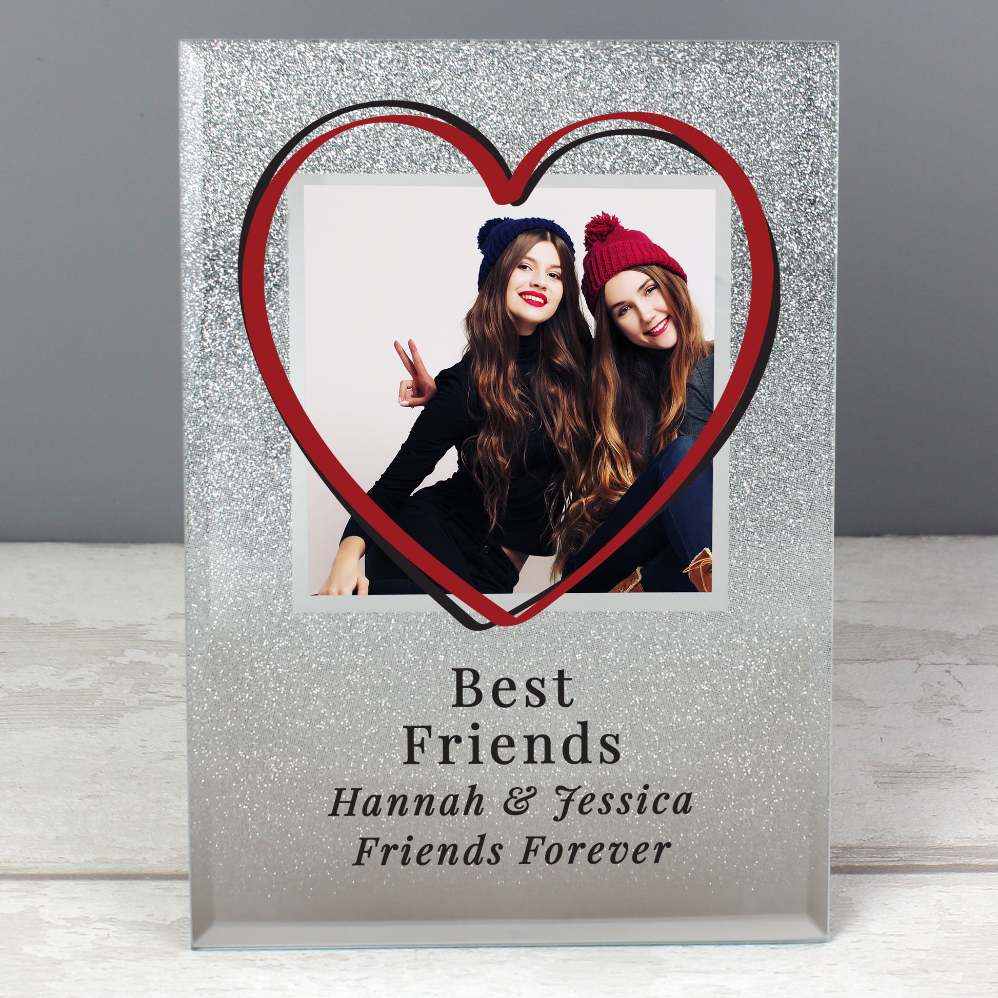 Heart-shaped photo frame with a photo of two people and personalised text 'Best Friends Hannah & Jessica Friends Forever' on a grey background.