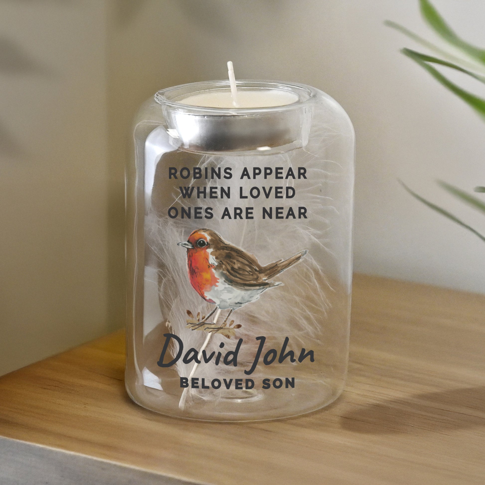 Candle in a jar with a robin design and text on a wooden surface