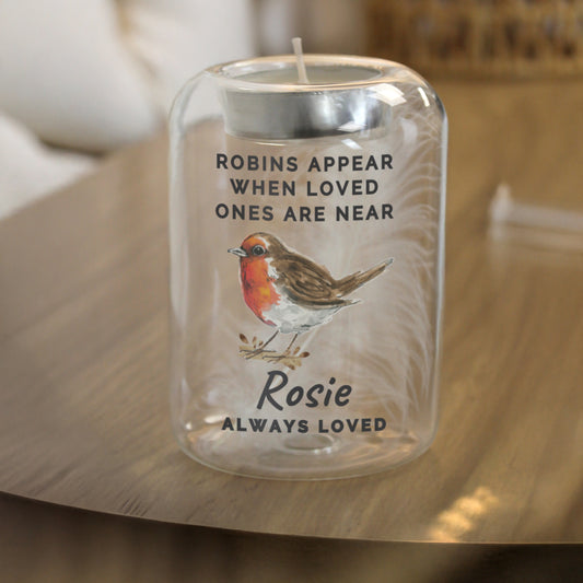 Candle in a personalised glass jar with a robin illustration and text on a wooden surface