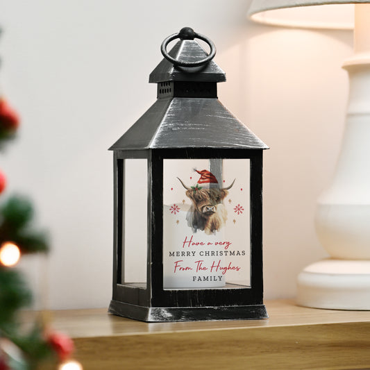 Black lantern with a personalised Christmas design featuring a cow wearing a Santa hat on a wooden surface.
