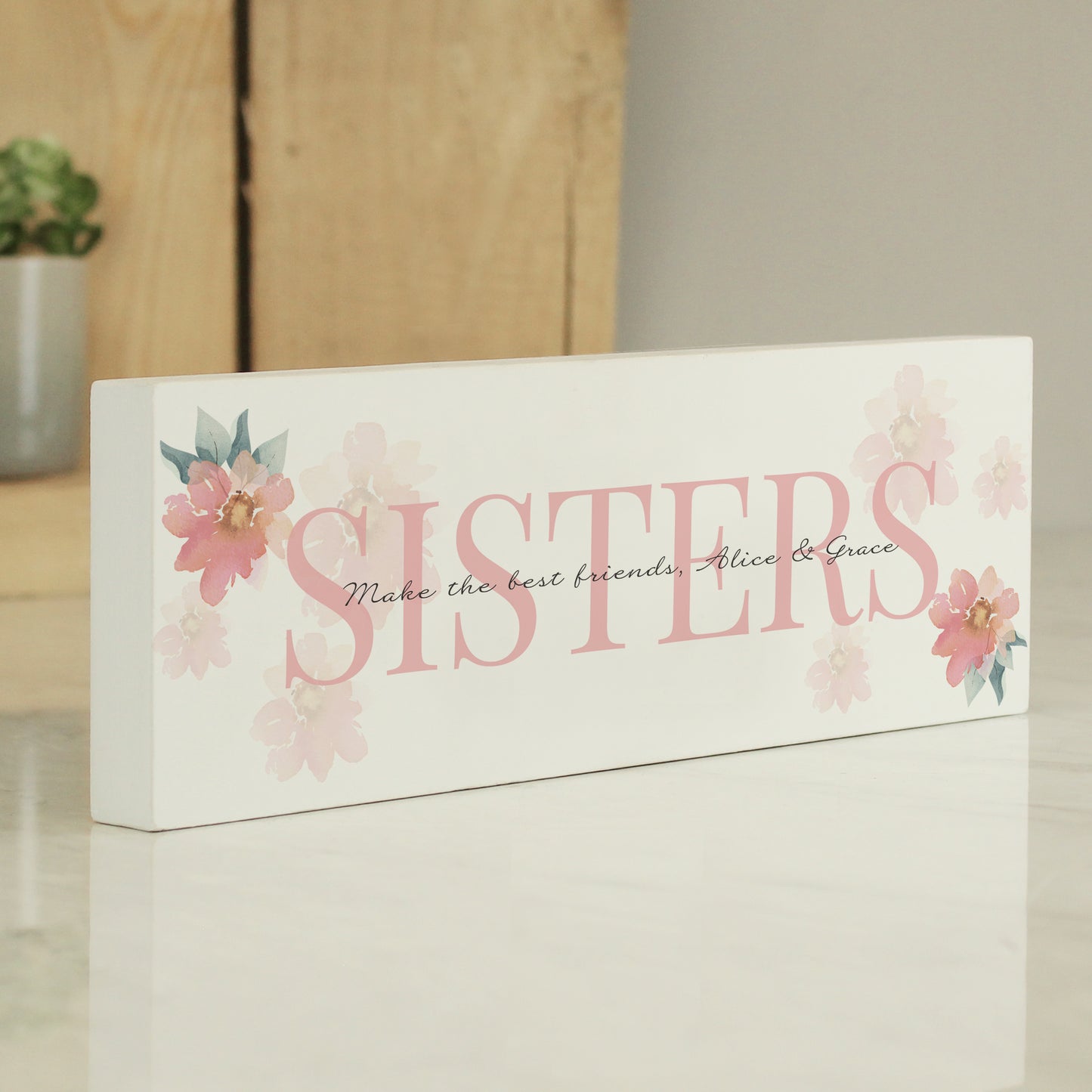 Decorative sign with 'SISTERS' and floral designs on a white background