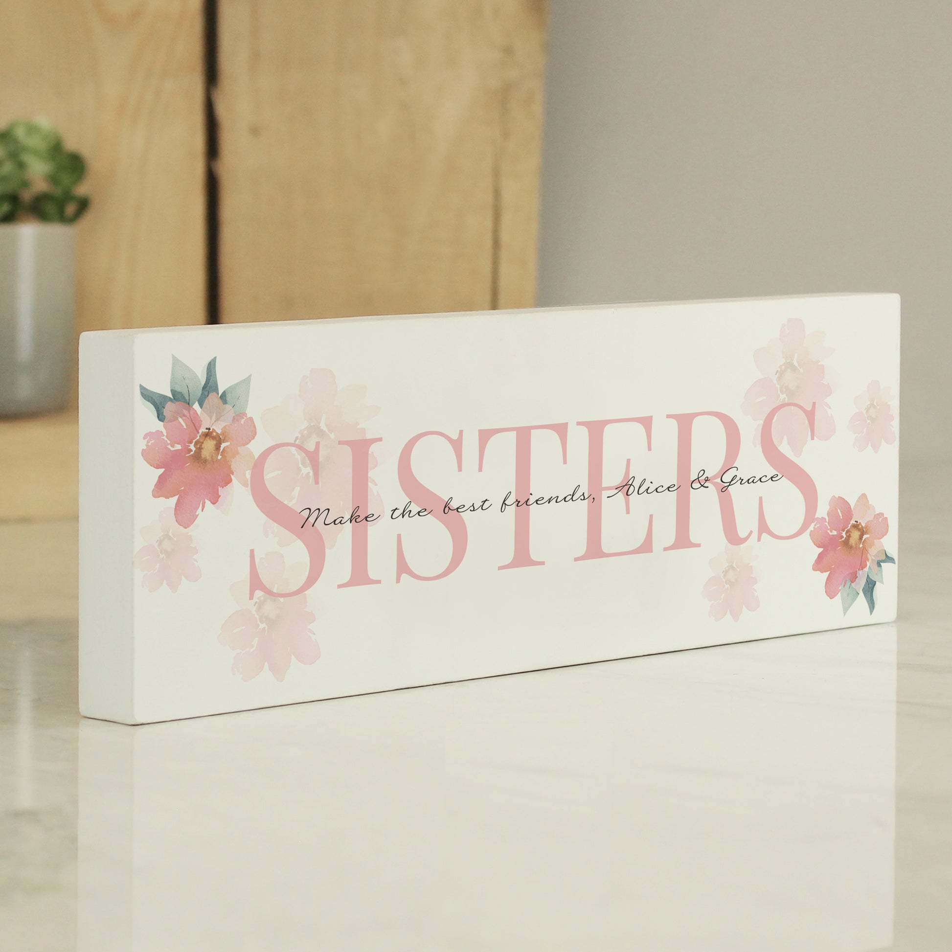 Decorative sign with 'SISTERS' and floral designs on a white background