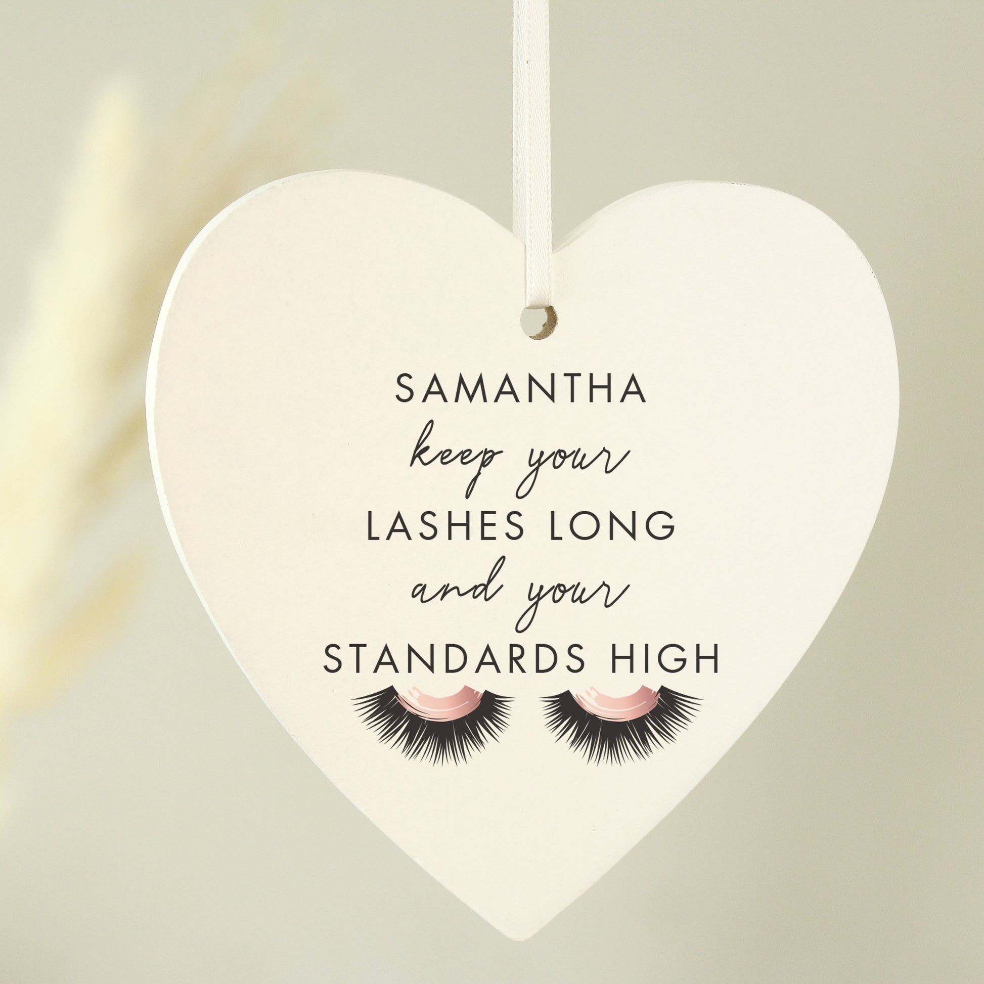 Heart-shaped hanging sign with eyelashes and personalised name on a neutral background