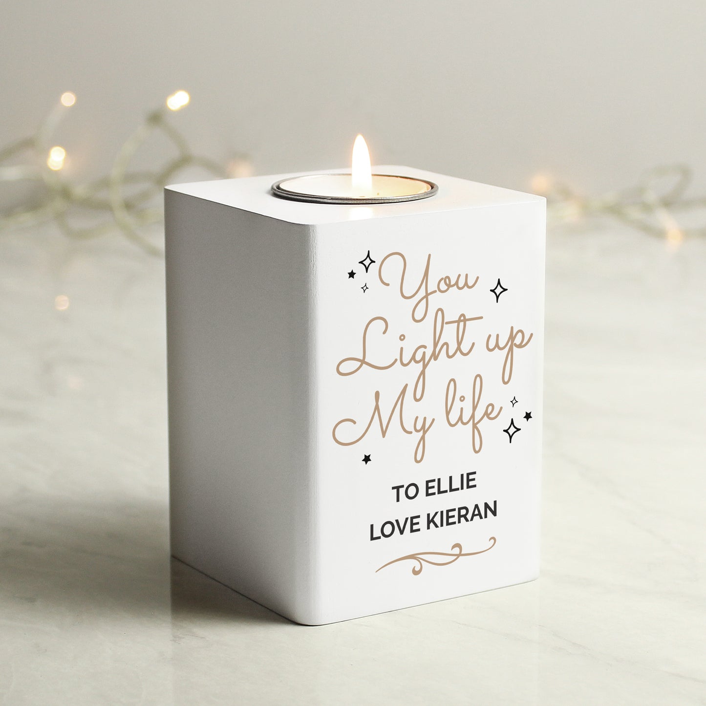 White candle holder with 'You Light up My Life' text, lit candle inside, on a neutral background.