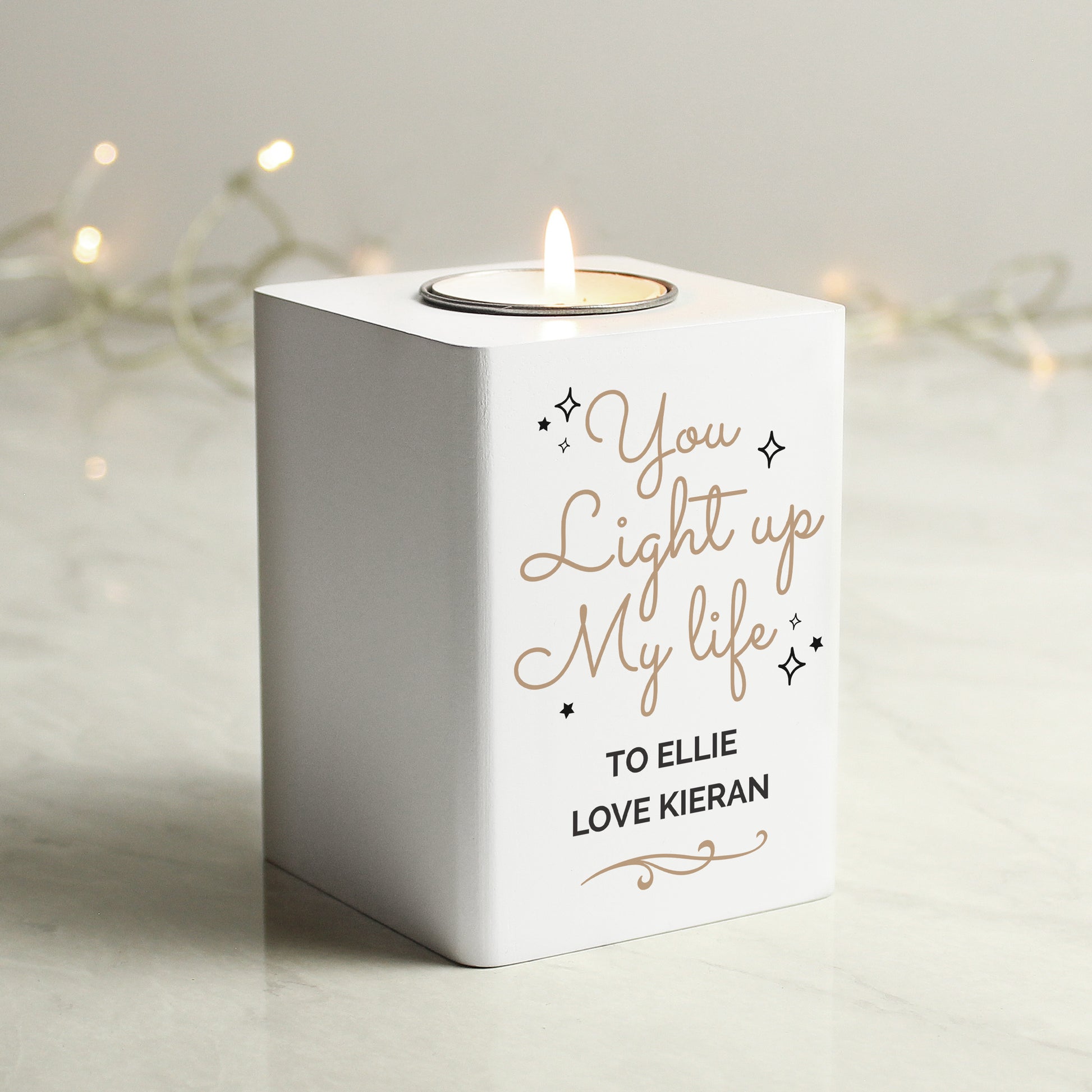 White candle holder with 'You Light up My Life' text, lit candle inside, on a neutral background.