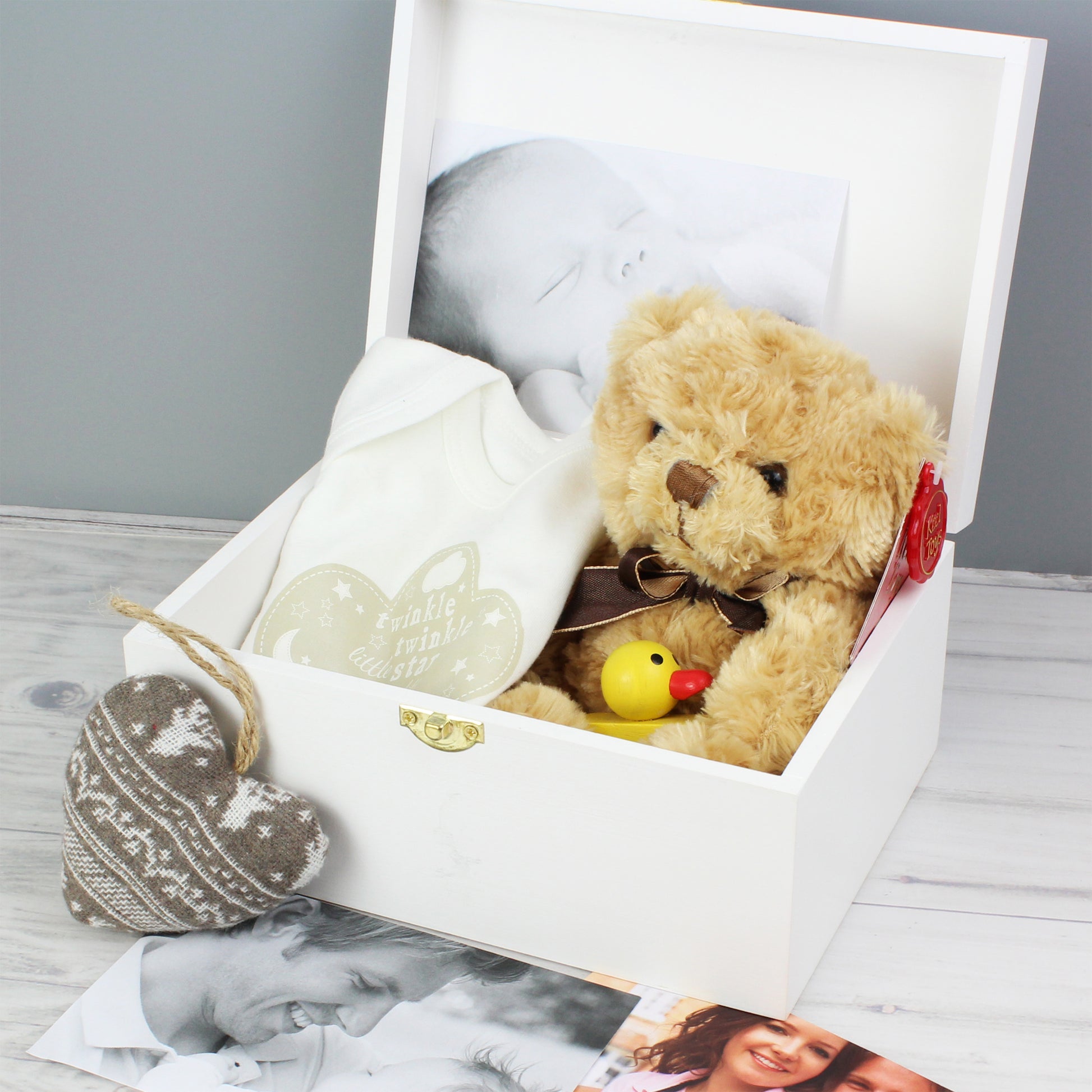 Teddy bear with a bow tie and rubber duck in a white box on a wooden surface.