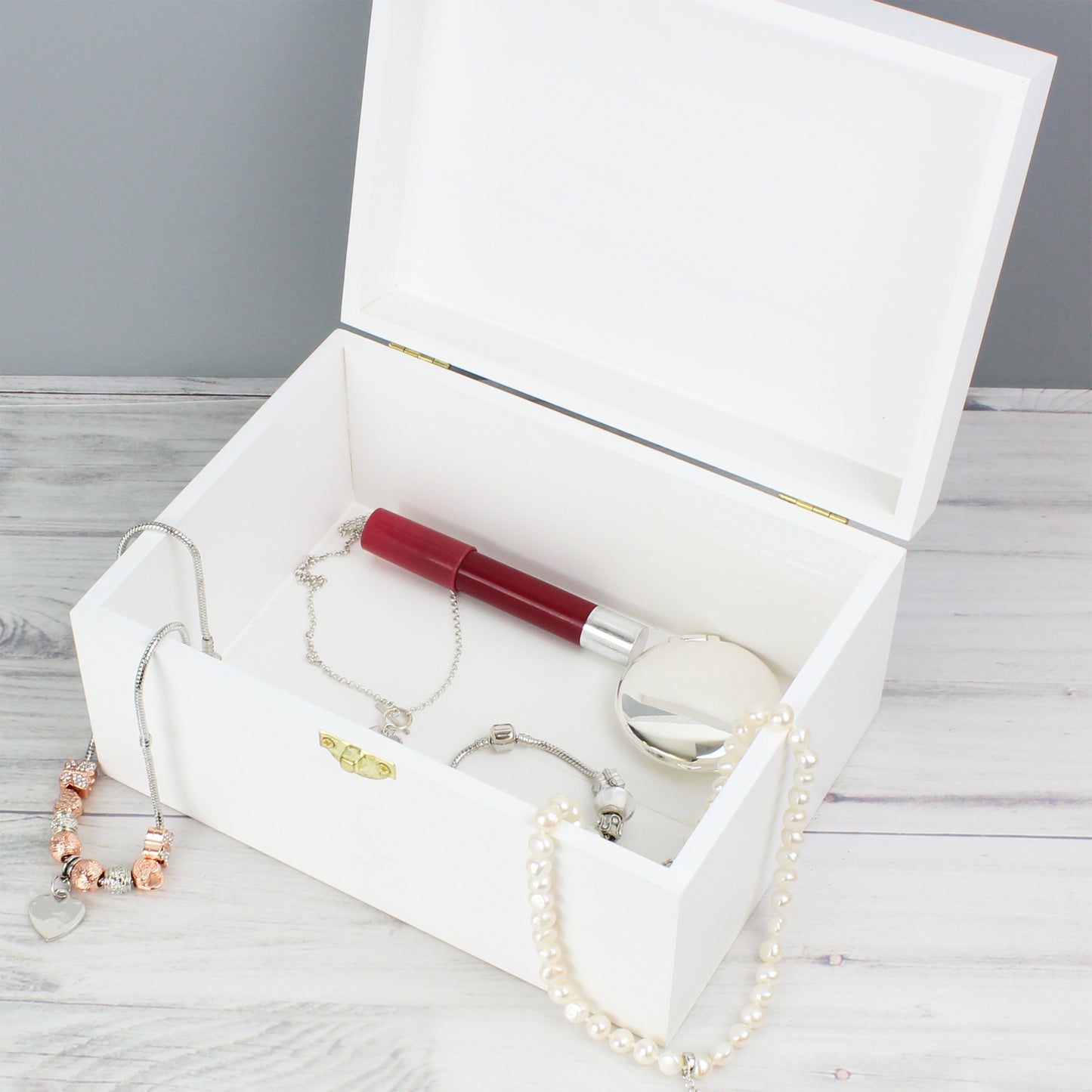 Jewelry set including a bracelet, necklace, and lip gloss in an open white box on a wooden surface.