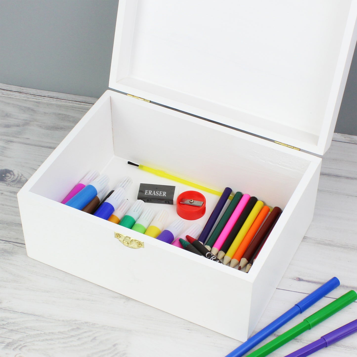 White pencil box with colorful markers, pencils, and an eraser on a wooden surface.