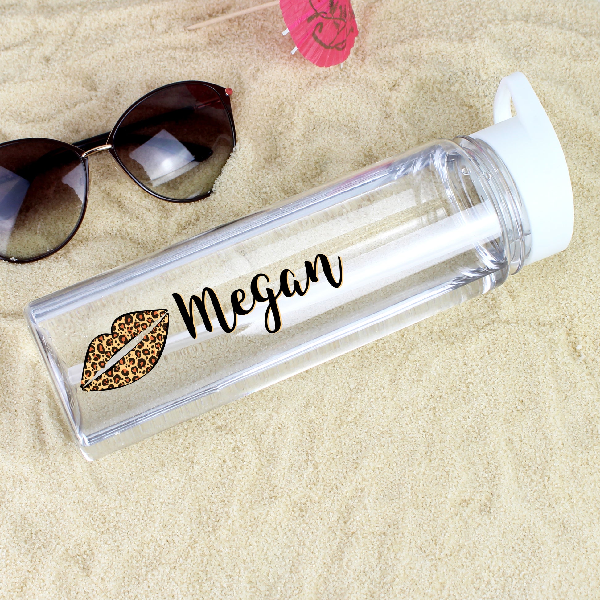 Clear water bottle with leopard print lips and 'Megan' on sand with sunglasses