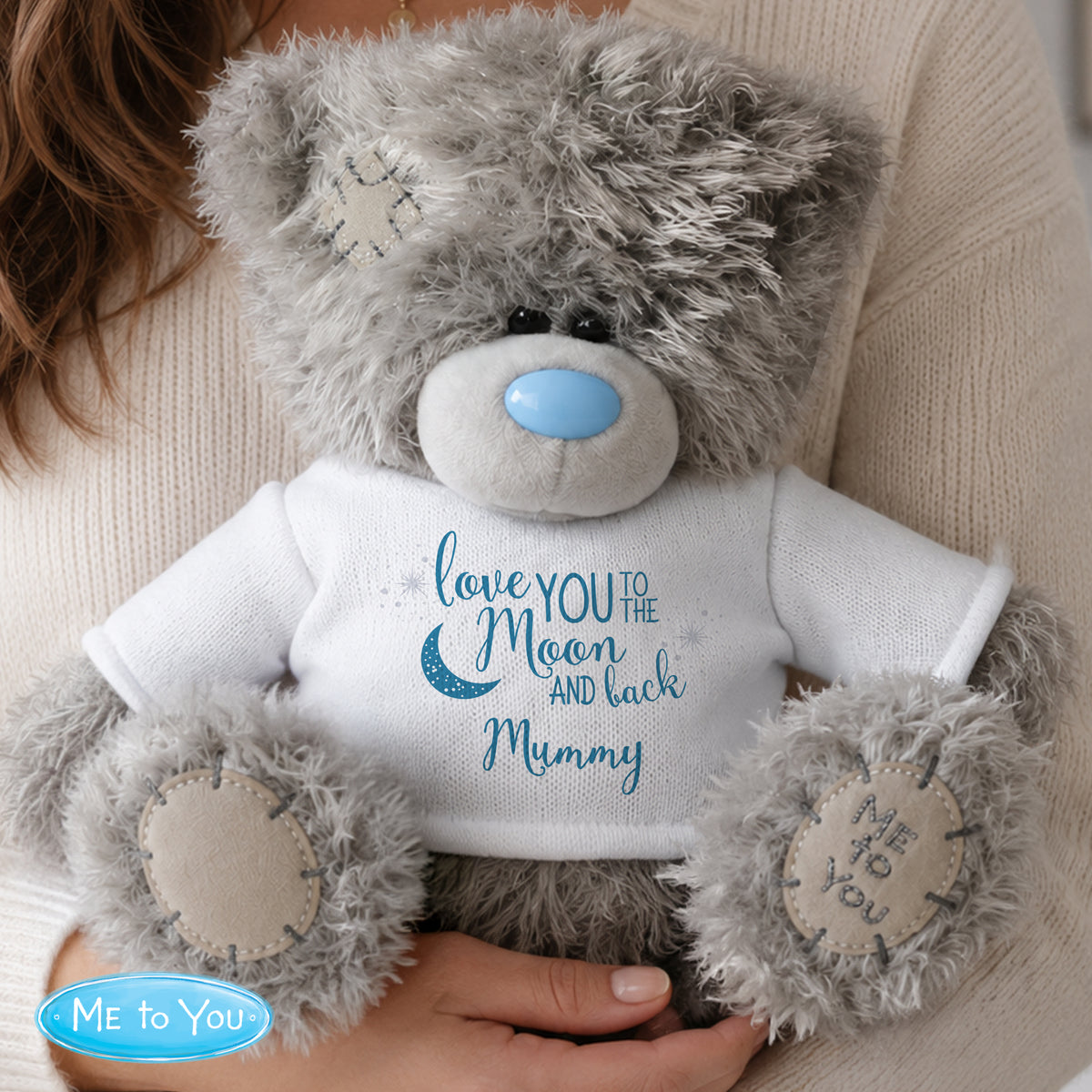Grey teddy bear with a white shirt reading 'love YOU to the MOON AND back Mummy' held by a person.