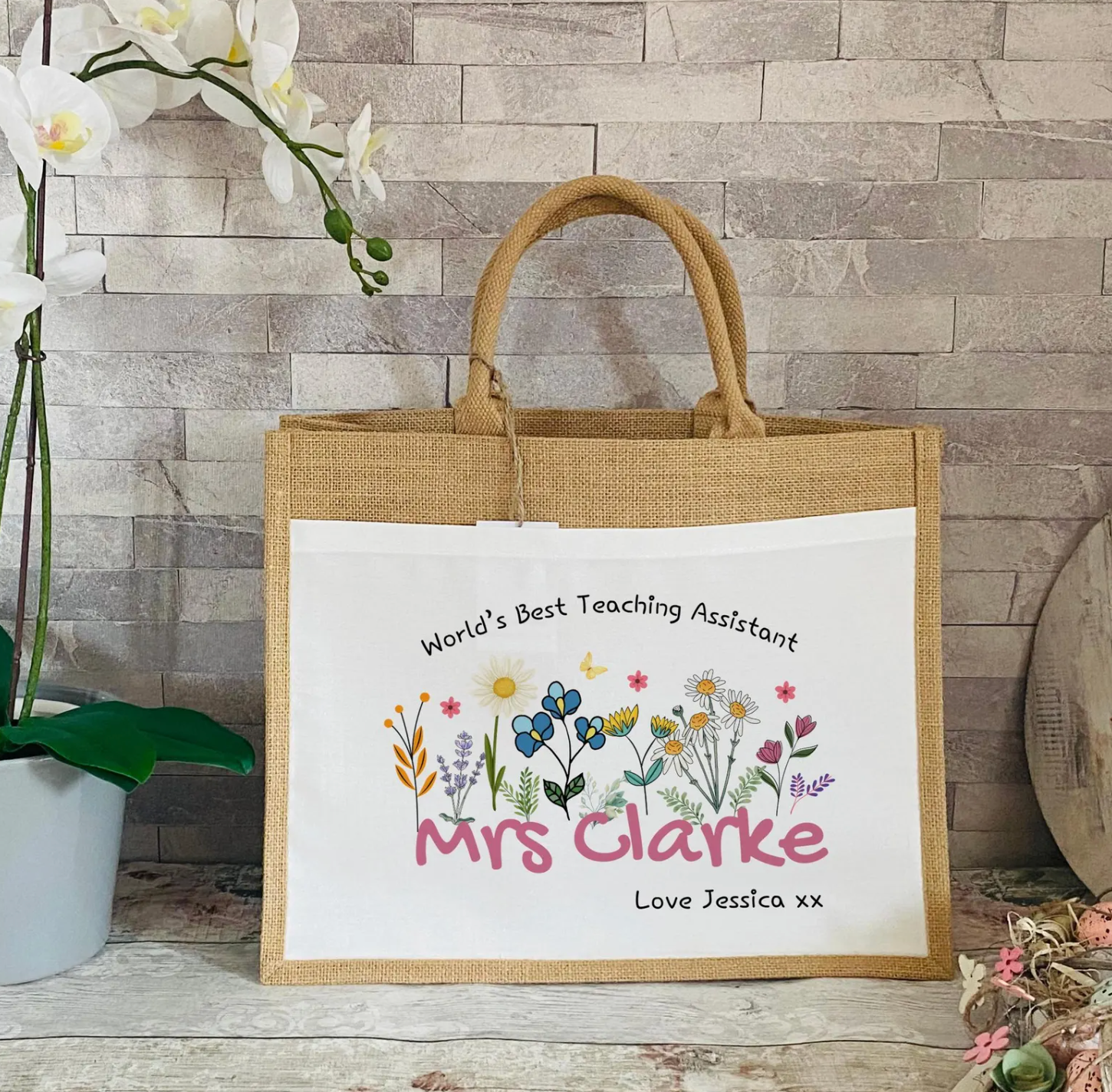 Jute bag with Worlds Best Teaching Assistant message against a wooden wall background