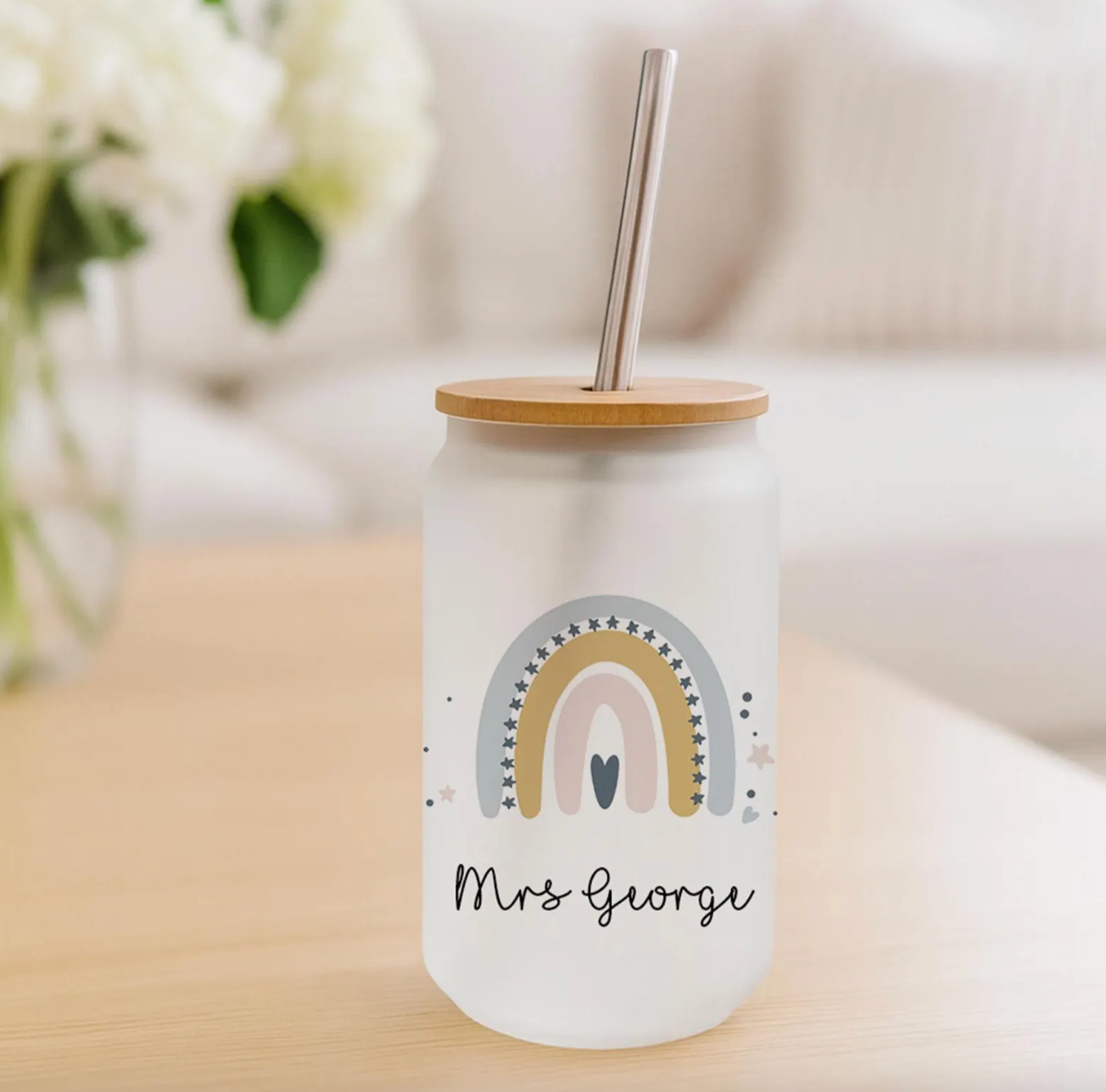 Glass teacher tumbler with rainbow design and 'Mrs George' text on a wooden surface.