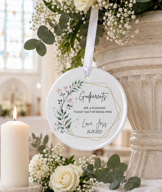 A round white hanging ornament with a white ribbon, printed with floral artwork and the words 'Godparents are a blessing thank you for being mine Love Jess 26.05.